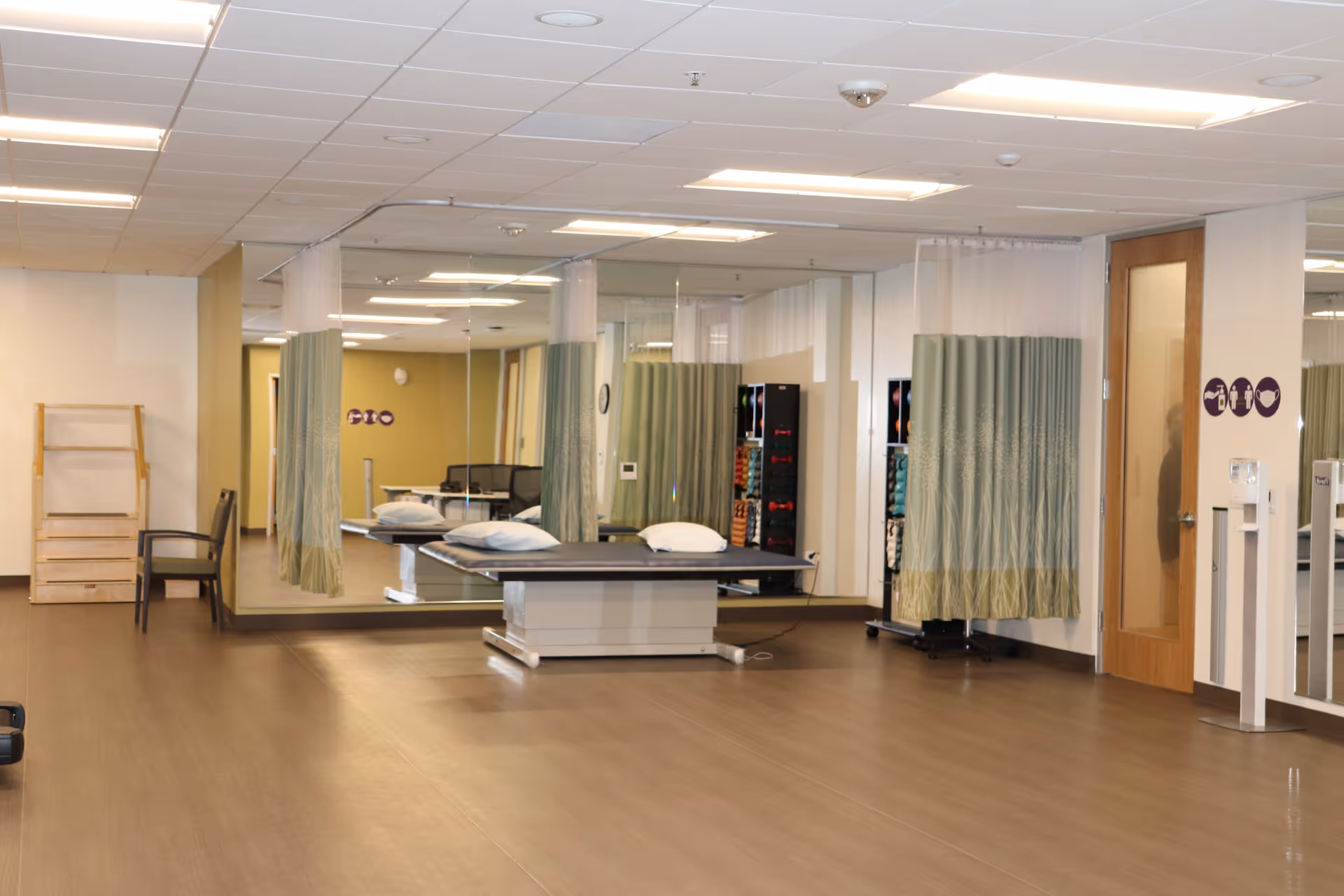 A spacious rehabilitation room with a treatment table, privacy curtains, and mirrored walls.
