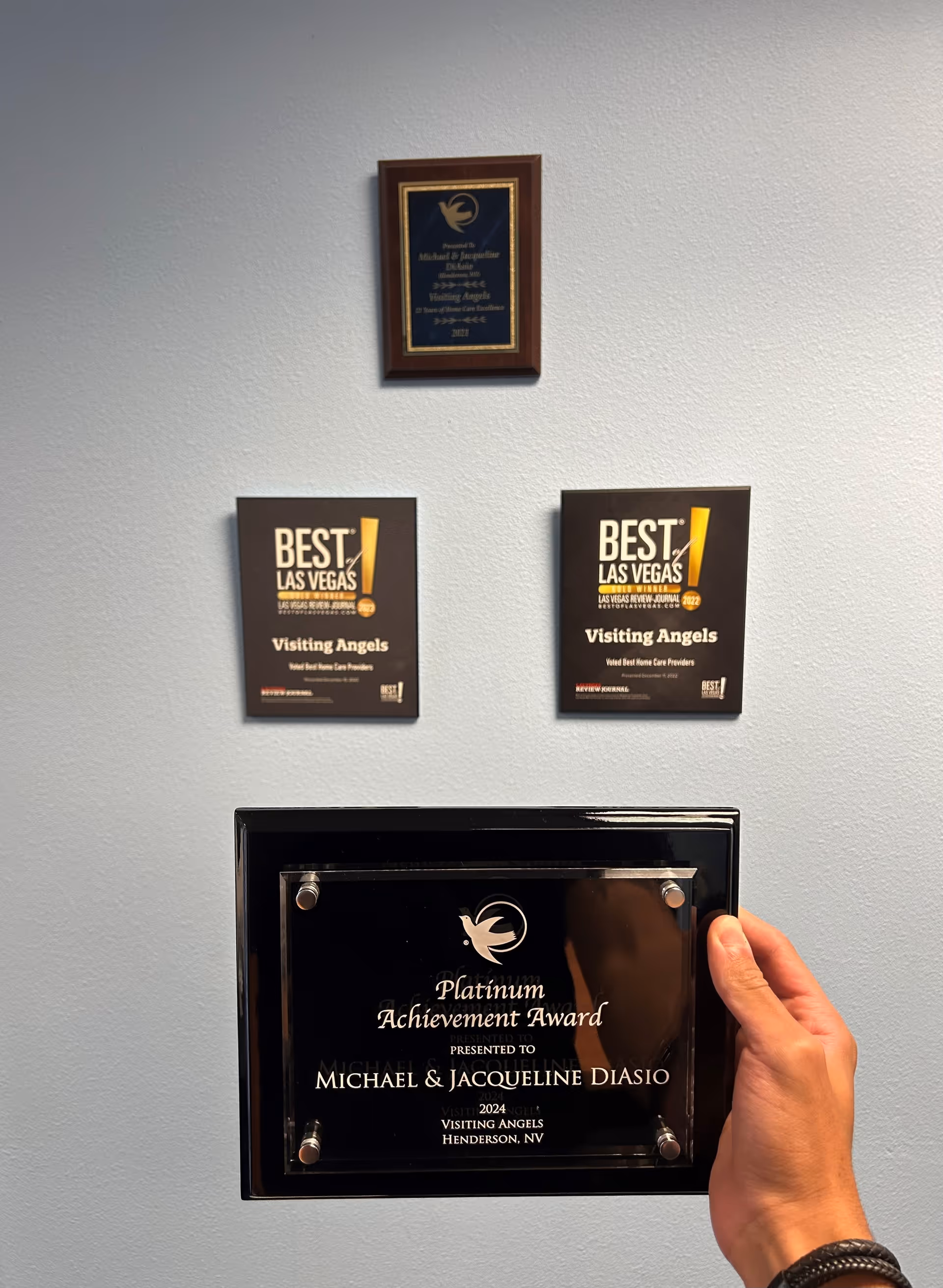 Wall-mounted awards and a hand gripping a glass plaque in a hallway display case.