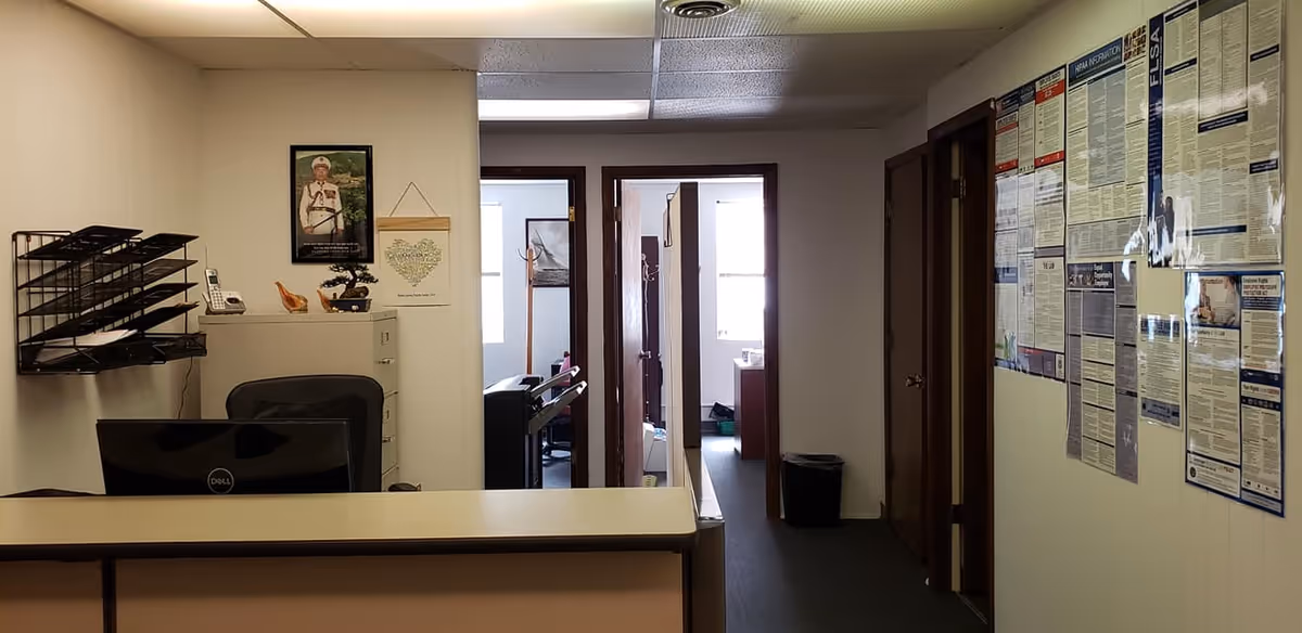 Reception desk in foreground, hallway with doors to rooms, and bulletin boards along wall.
