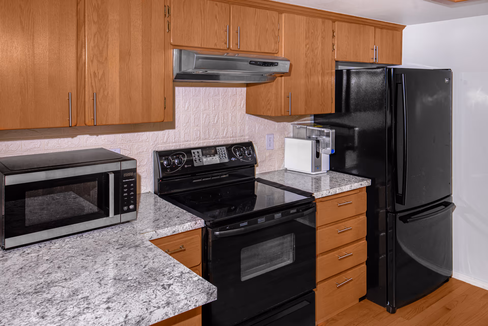 Compact kitchen with wooden cabinets, granite countertops, a microwave, and black appliances.