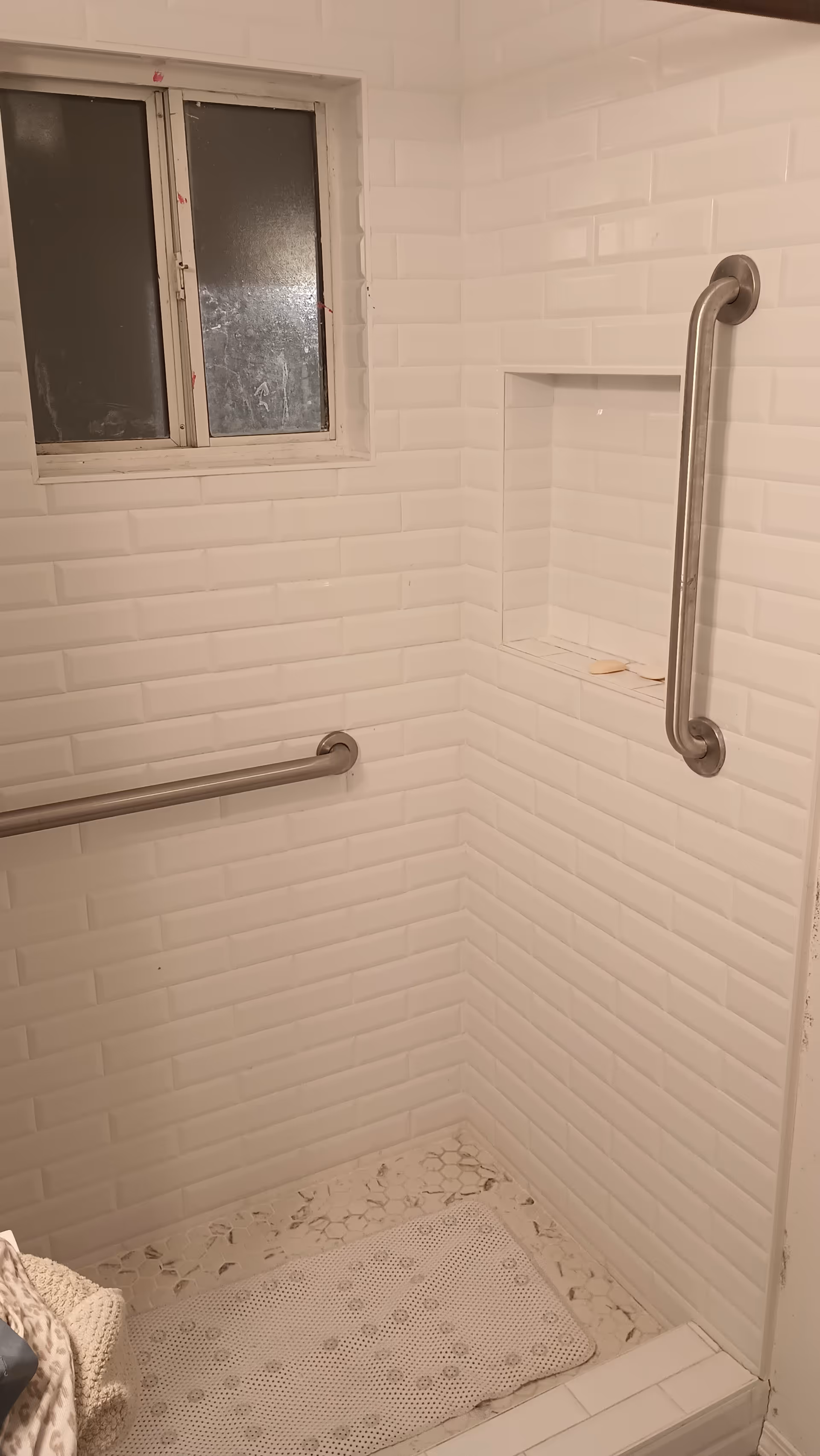 Small tiled bathroom shower with grab bars, a recessed shelf, and a frosted window.
