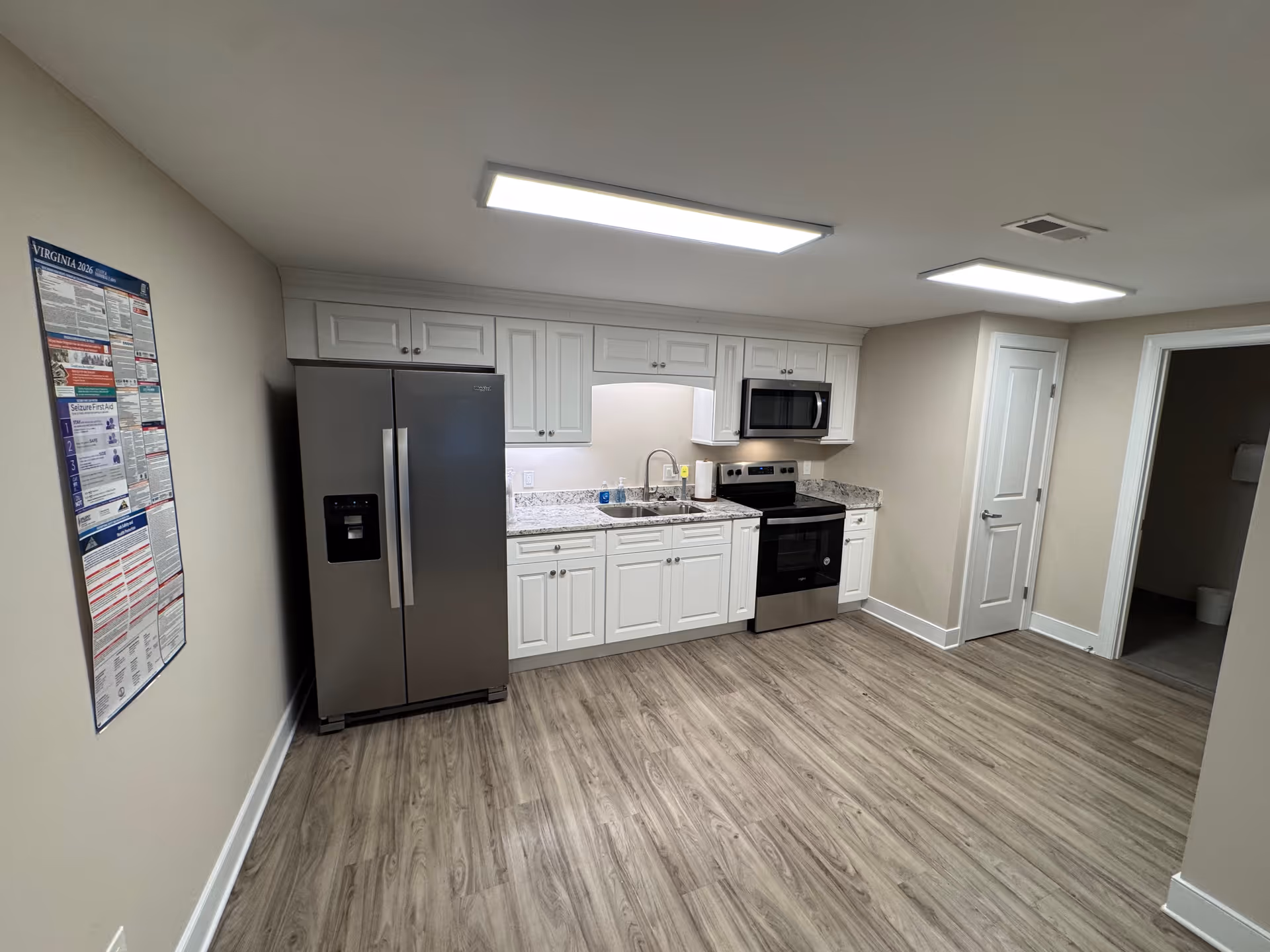 Modern kitchen with white cabinets, stainless steel appliances, and laminate flooring.