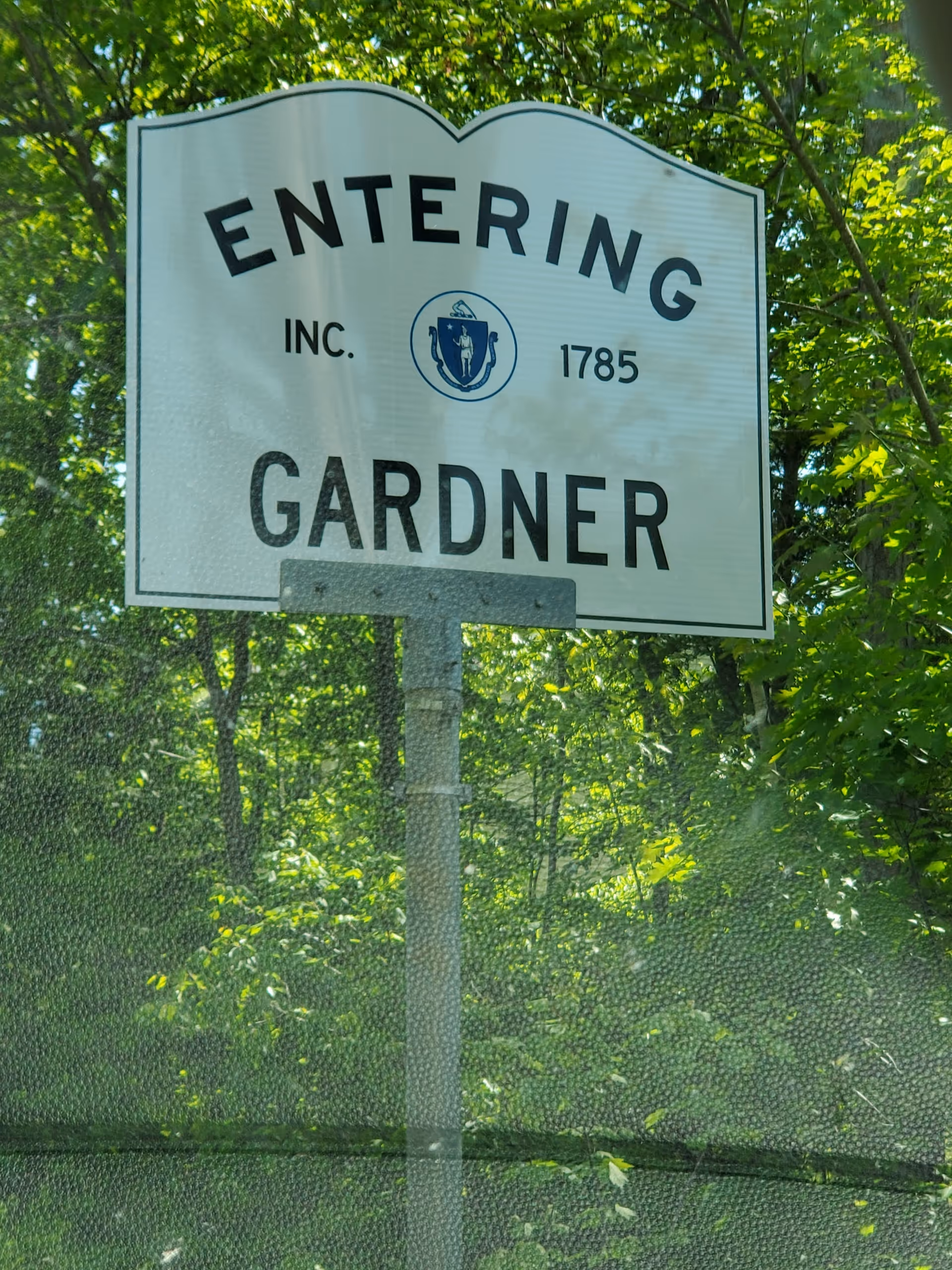 A large white road sign reading Entering Gardner with green trees behind.