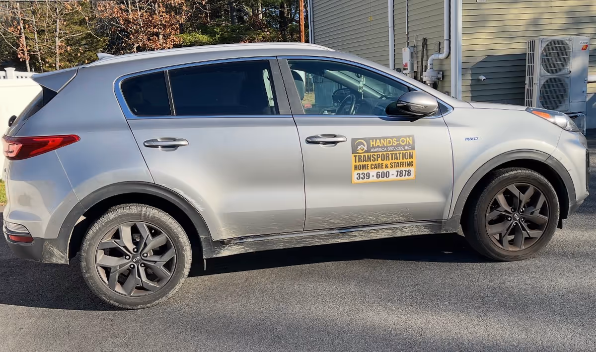 Silver SUV with Hands-On Transportation Home Care & Staffing sign parked beside a facility exterior.
