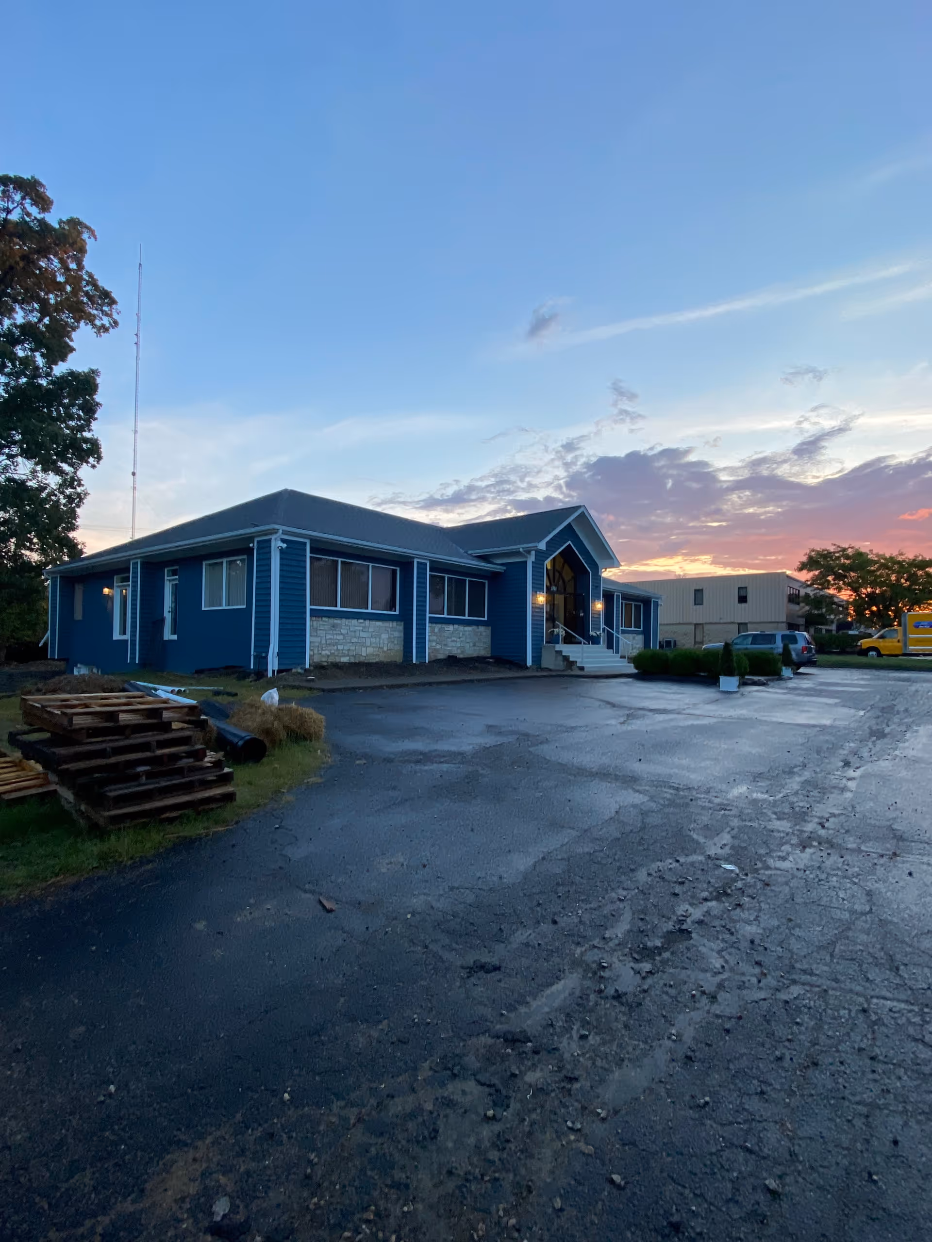 Blue single-story senior living facility exterior at sunset with a paved driveway