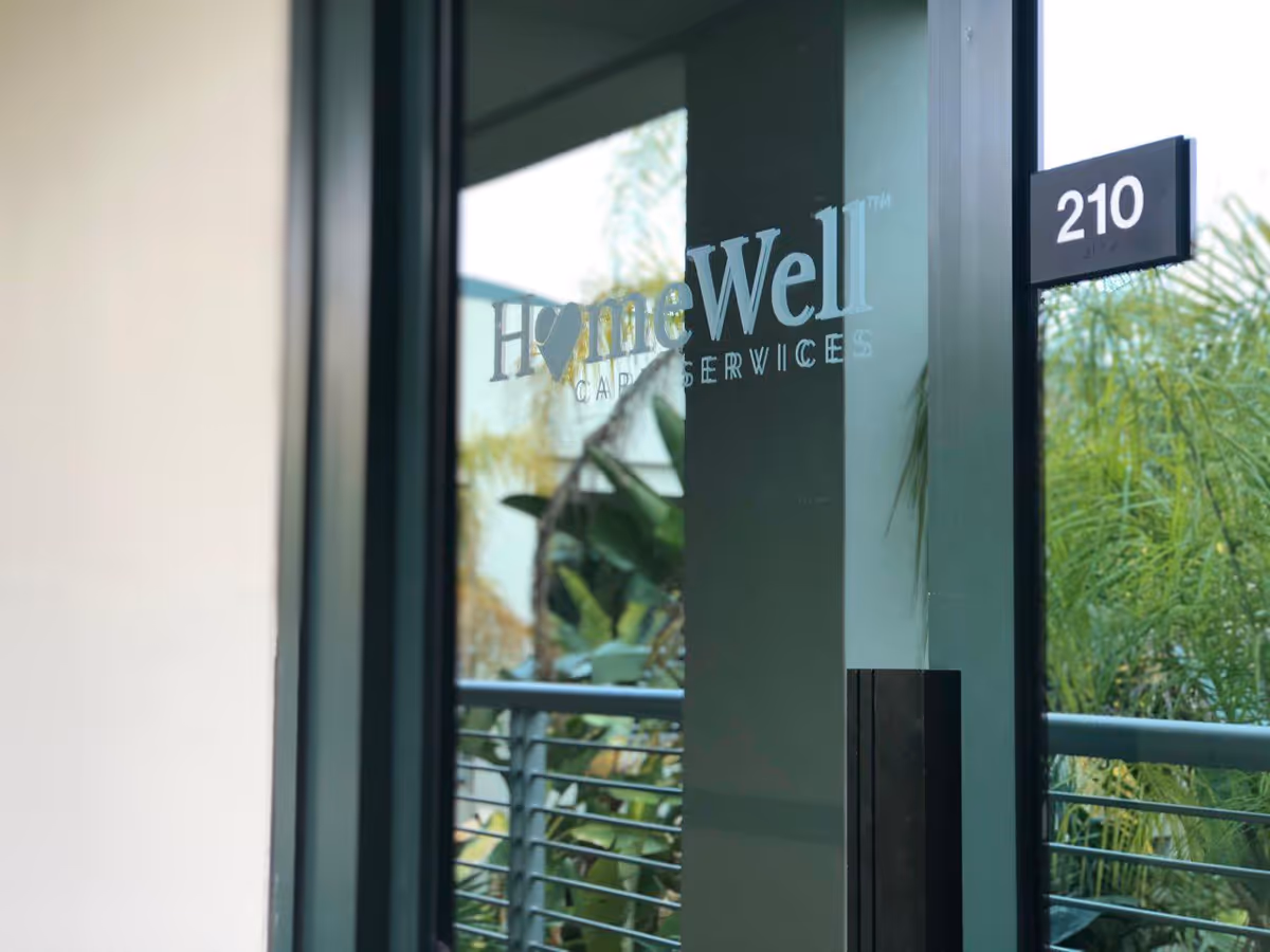 Glass entrance door displays HomeWell Care Services sign and 210 plaque.