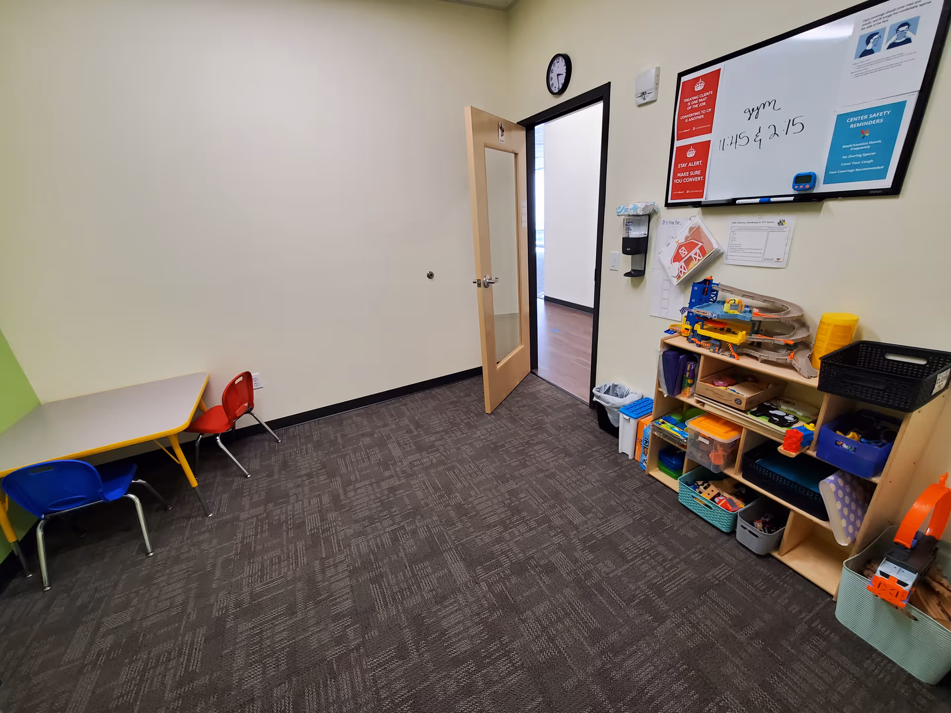 Colorful playroom corner with table, chairs, shelves, and toy organization near a doorway.