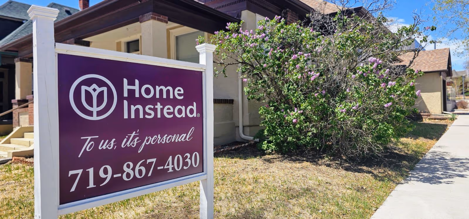 Front exterior of a Home Instead facility with a purple sign and sidewalk.