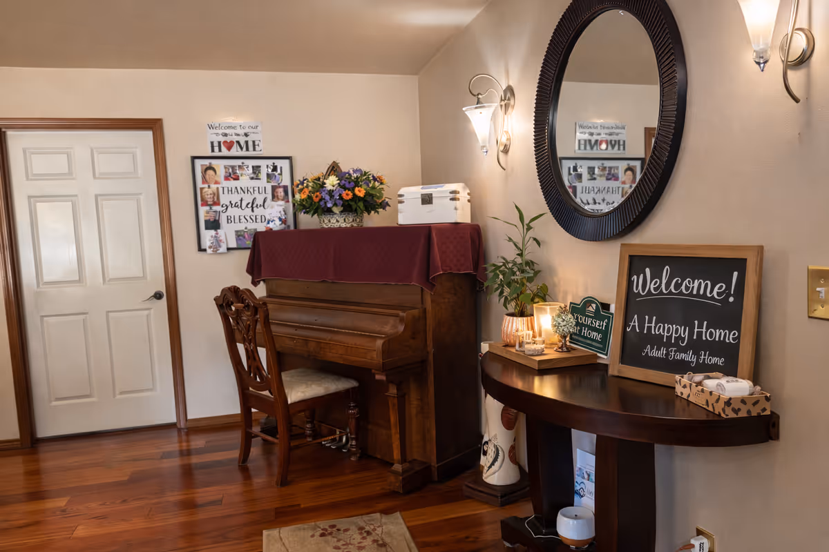 Cozy entry-style living area with a piano, round mirror, framed signs, and a console table.