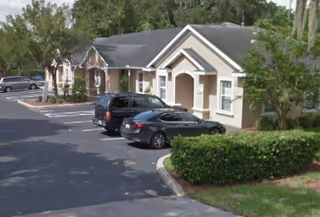 Exterior view of a single-story senior living facility with a parking lot and cars.