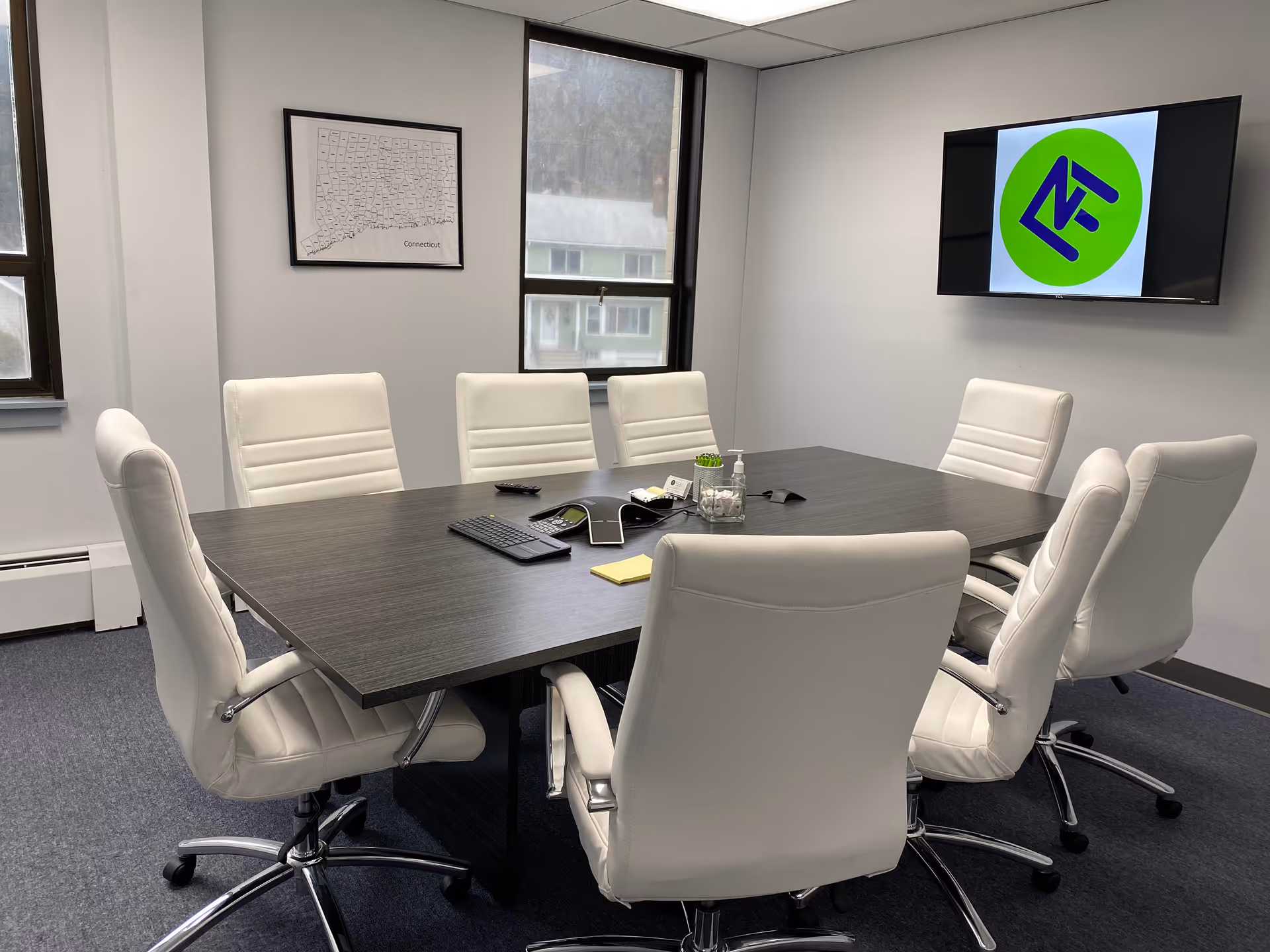A modern conference room with a dark wood table and white leather chairs.