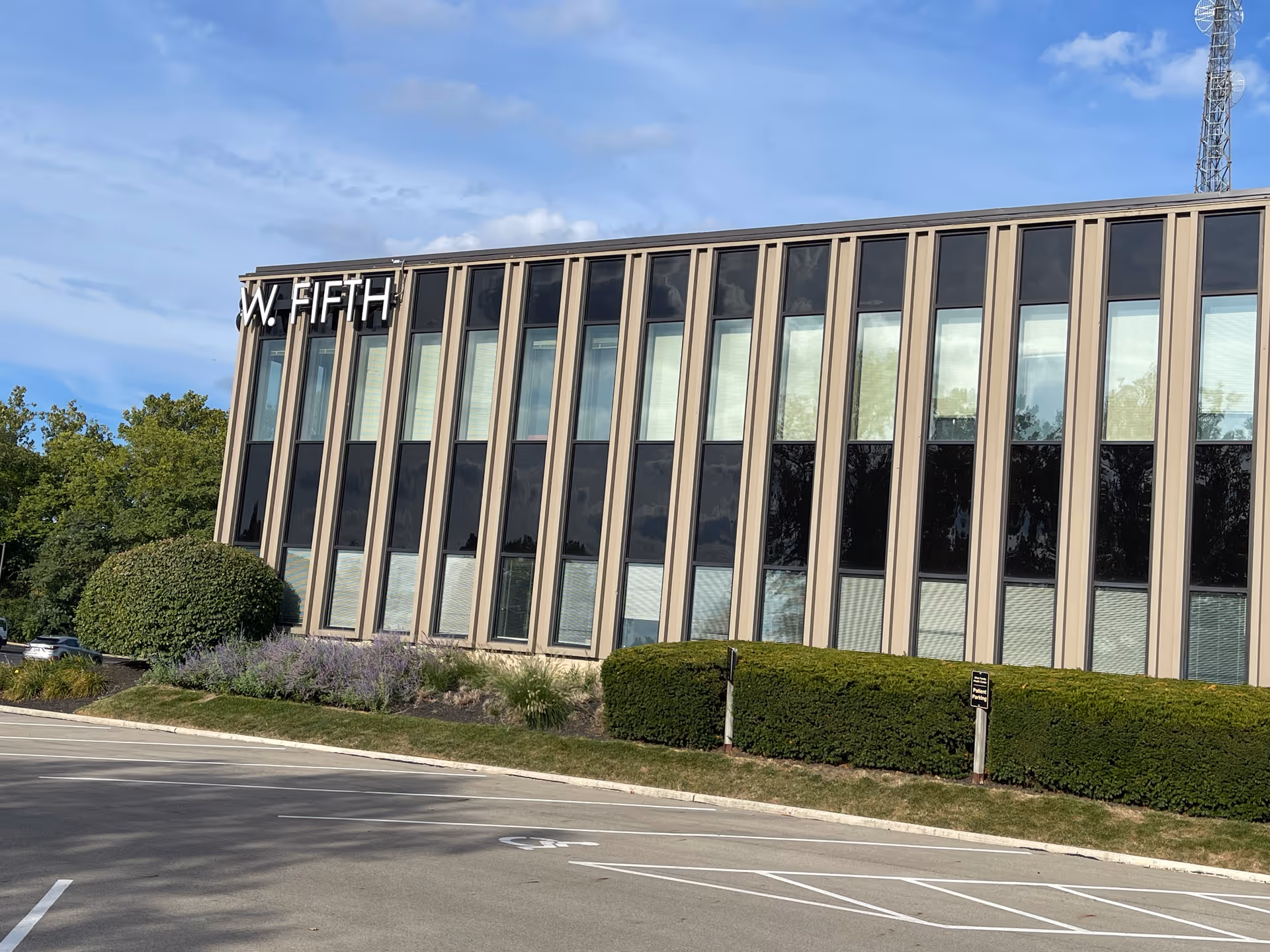 Modern glass-front building with trimmed hedges and a parking lot.