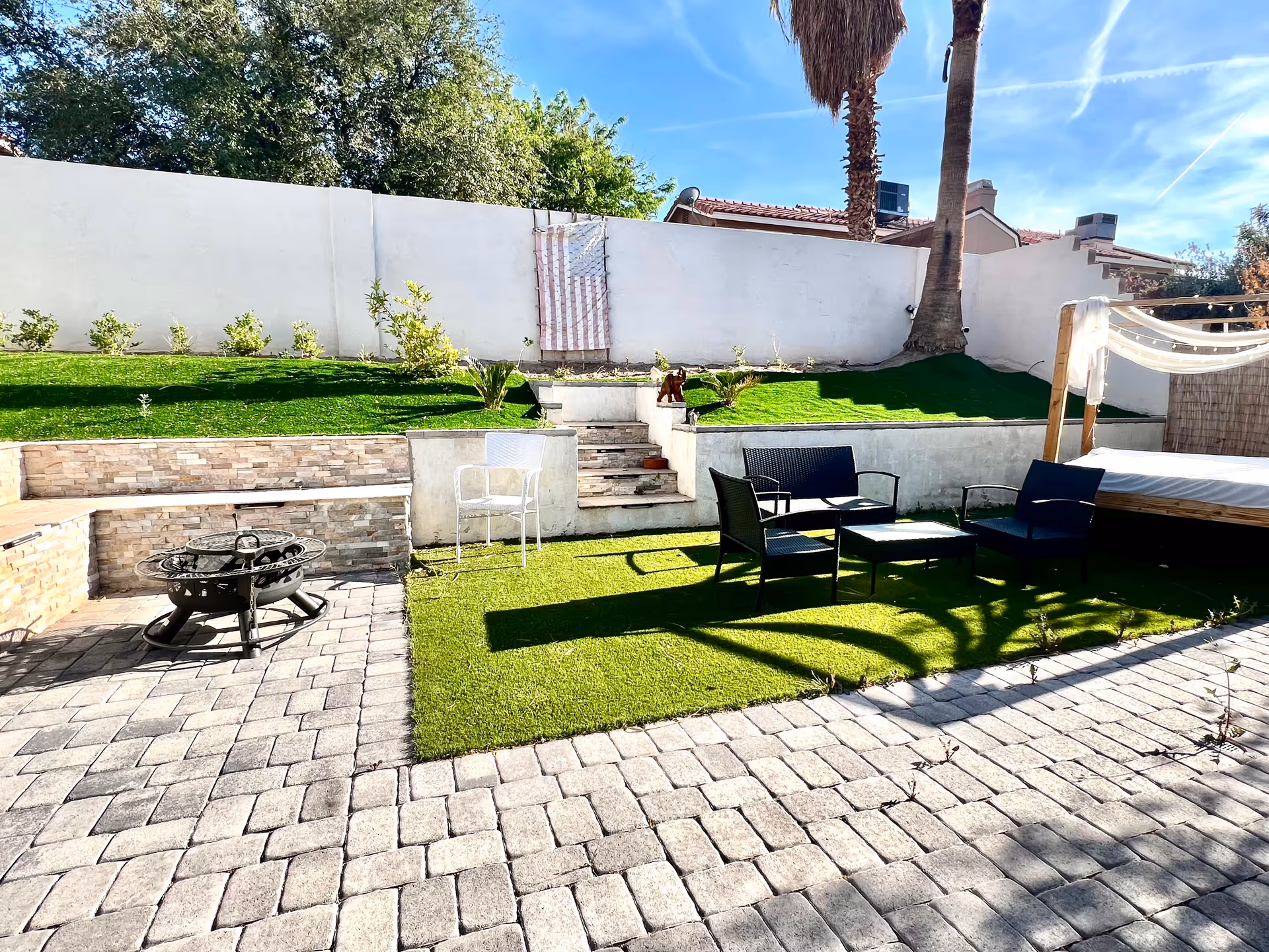 Outdoor courtyard with seating, fire pit, lawn, and paved patio against white wall.