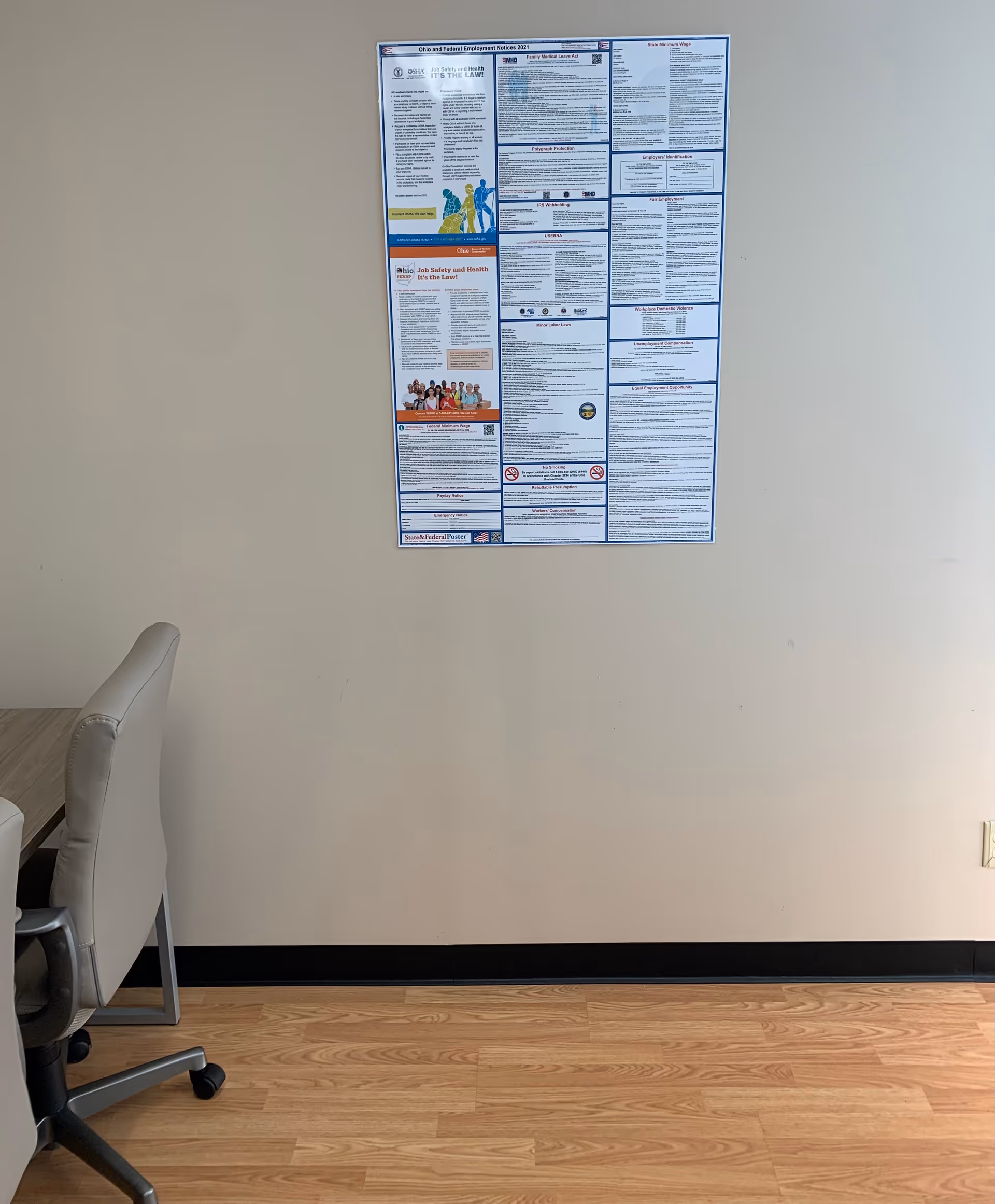 Interior office-like space with a wall-mounted poster, partial desk chair, and wooden floor.