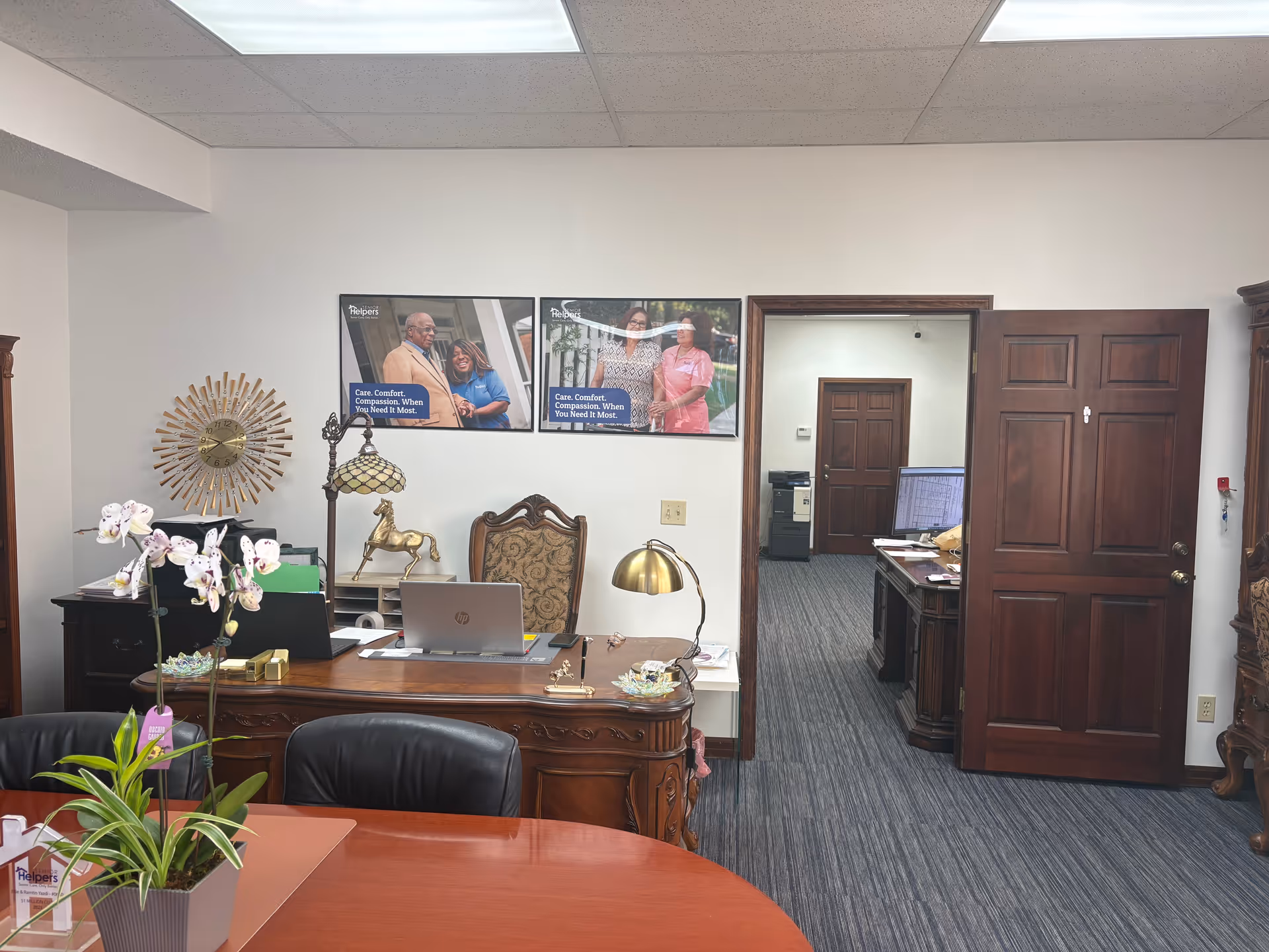 Office reception area with wooden desk, chairs, computer, and framed posters.