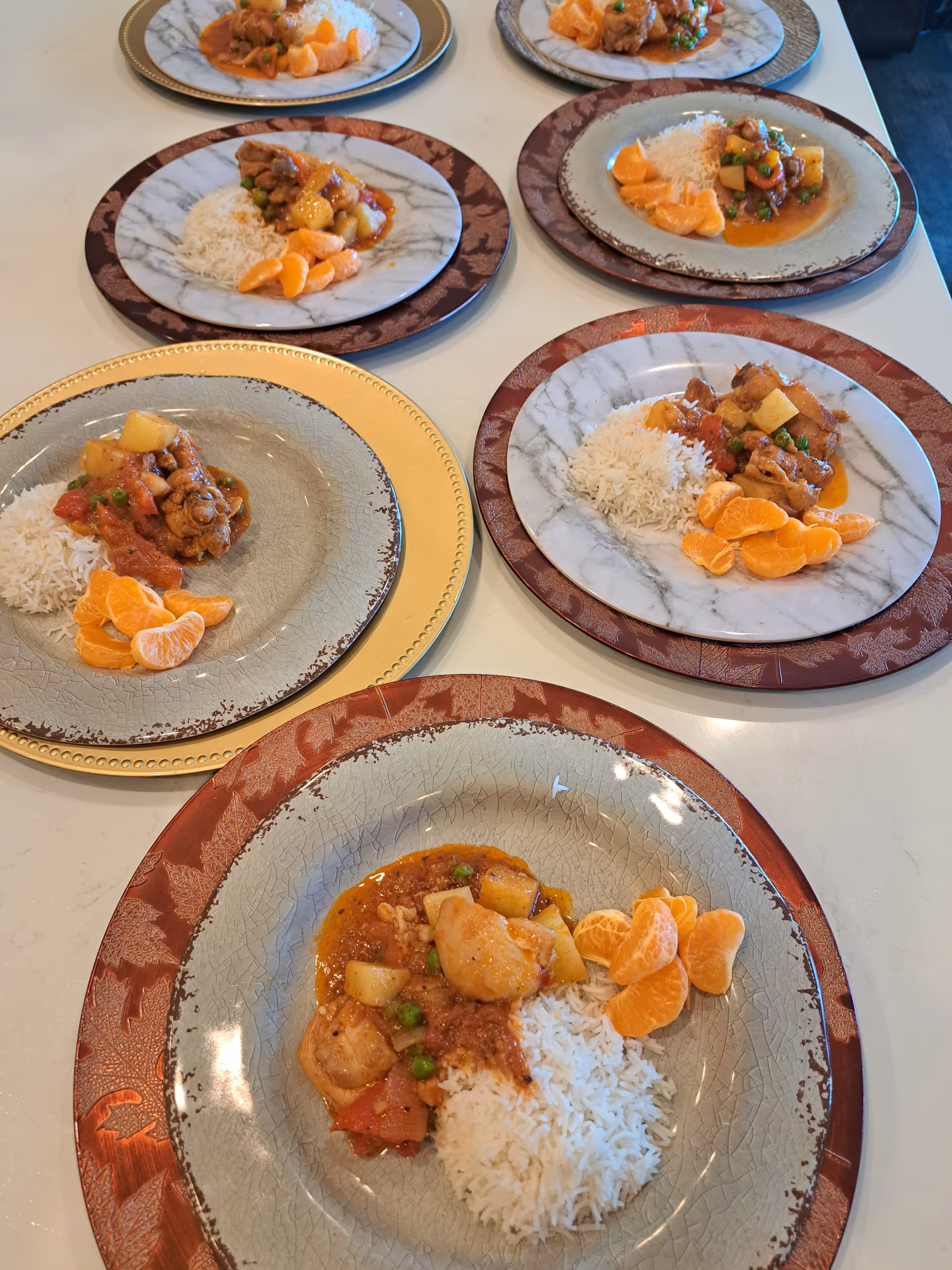 Several marble-patterned plates hold meals of rice, meat, and oranges.