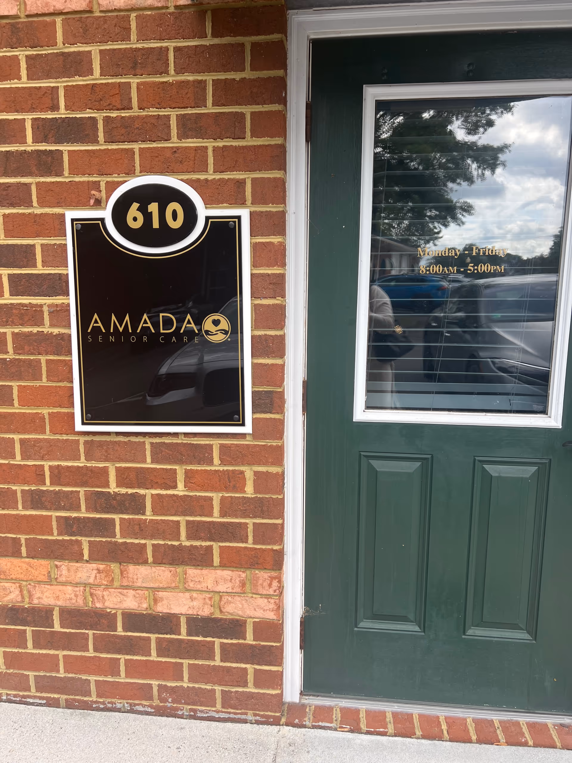 Exterior brick wall featuring Amada Senior Care sign and green door entrance.