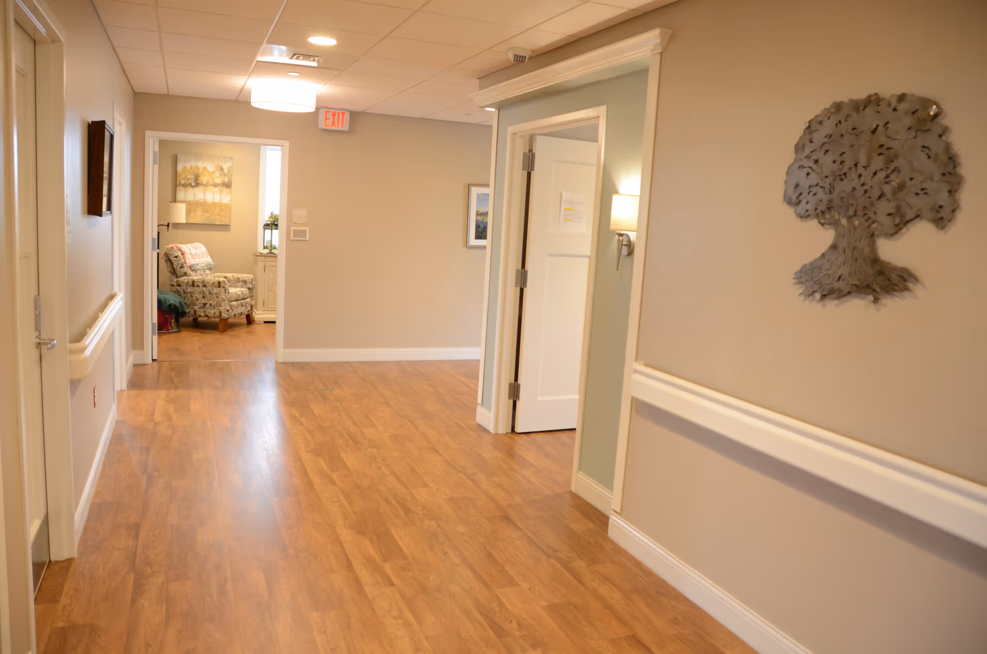 A bright hallway in a senior living facility with wood floors and a seating area.