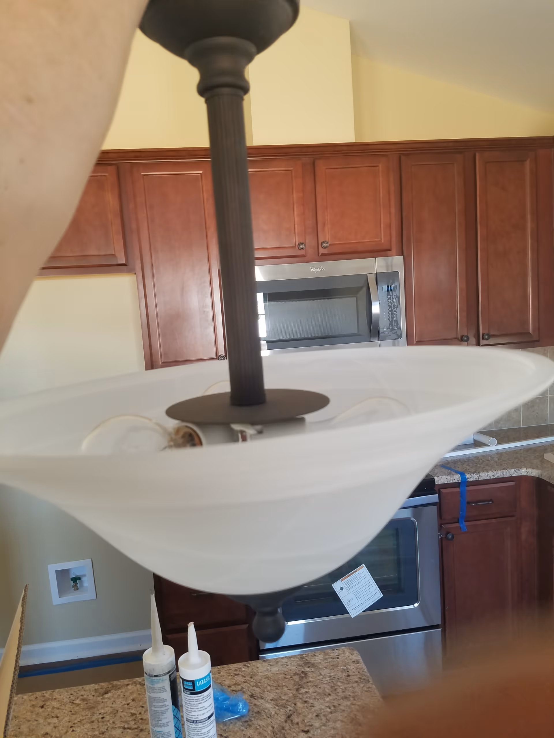Close-up view of a kitchen ceiling light fixture over granite counter and wooden cabinets.