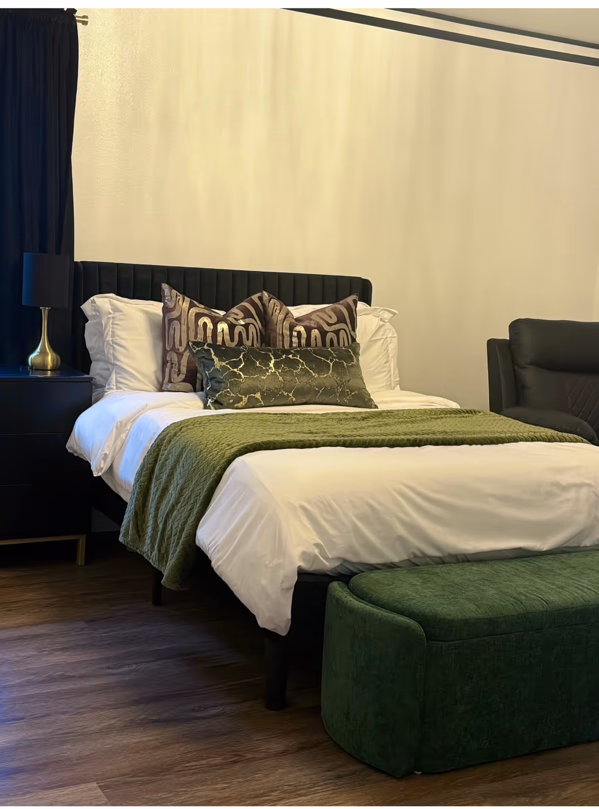 Contemporary bedroom with a large bed, dark headboard, pillows, and green throw.