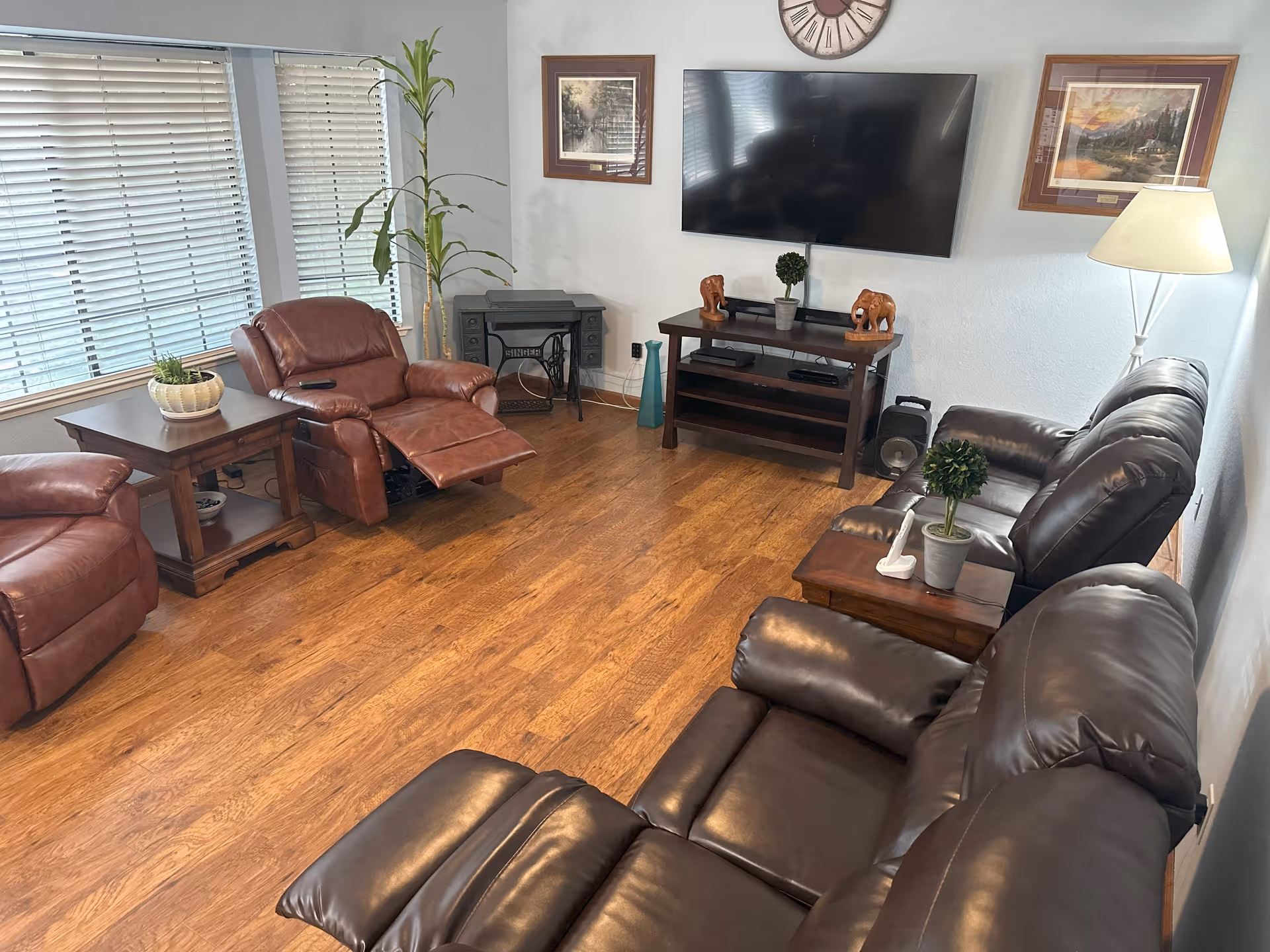 Cozy living room with leather couches, chairs, a TV, and wooden tables.