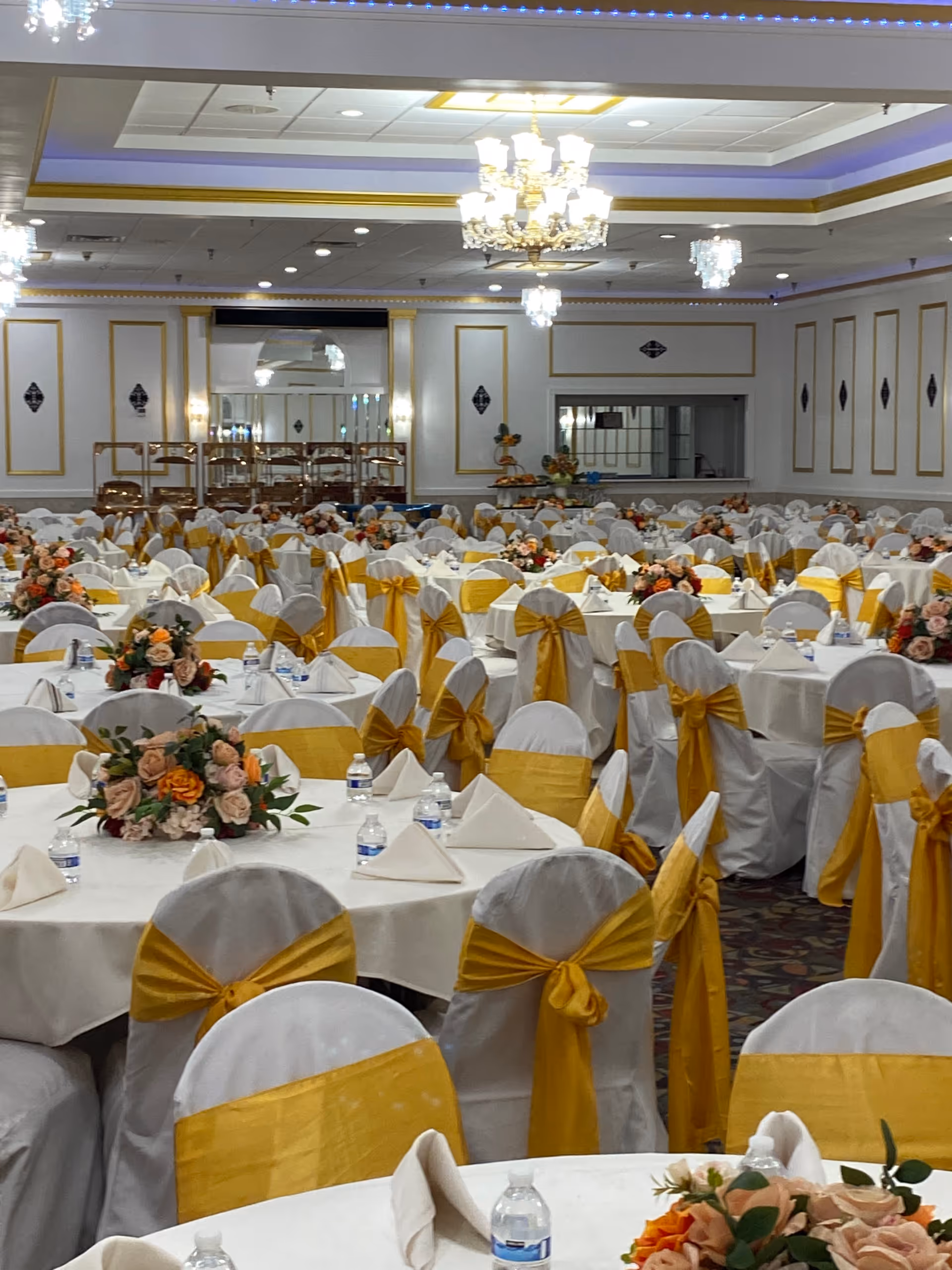 Elegant banquet hall with round tables, white linens, and gold chair sashes.