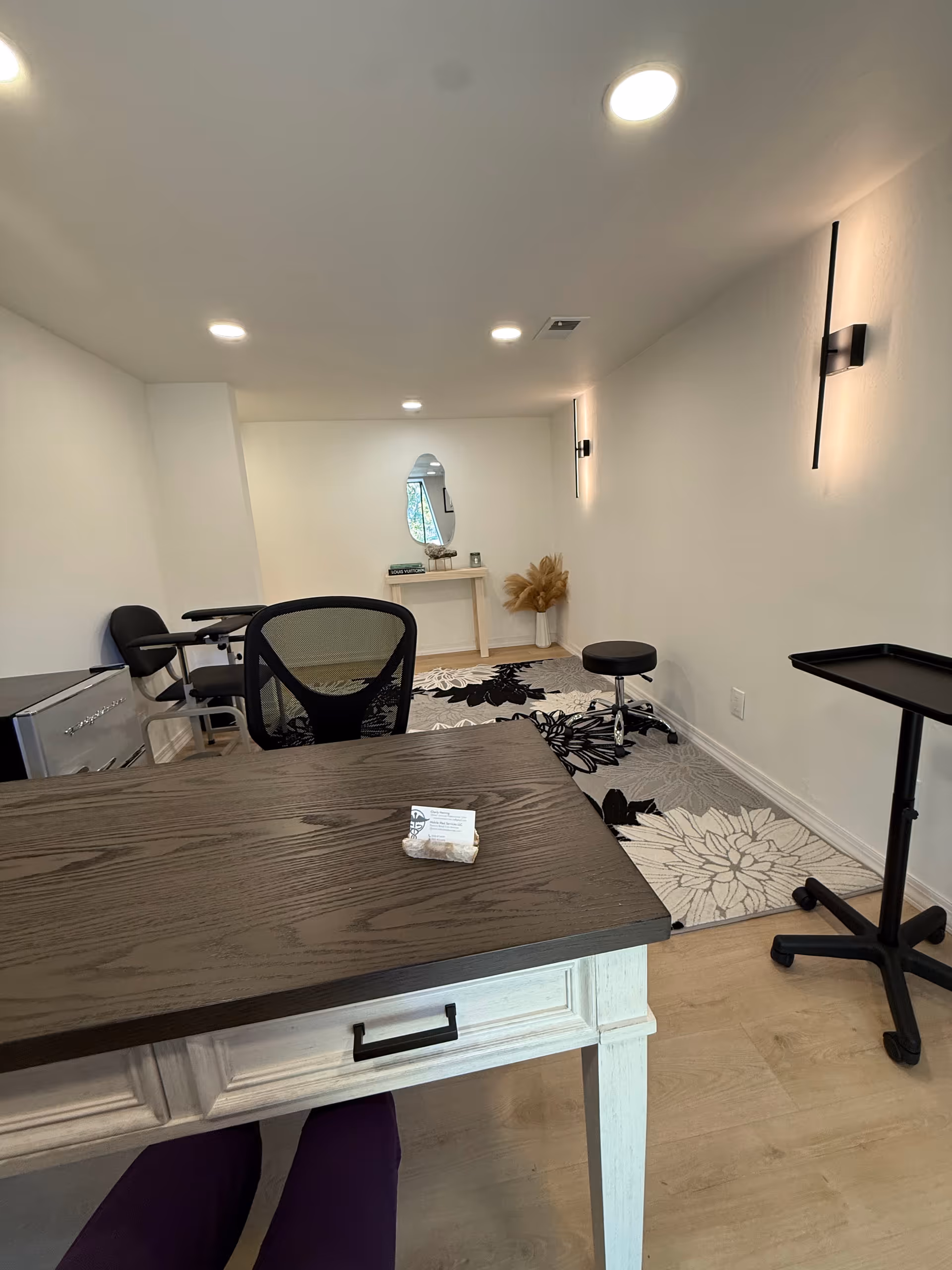 Bright, minimal interior office space with desk, chair, rug, mirror, and small stool.