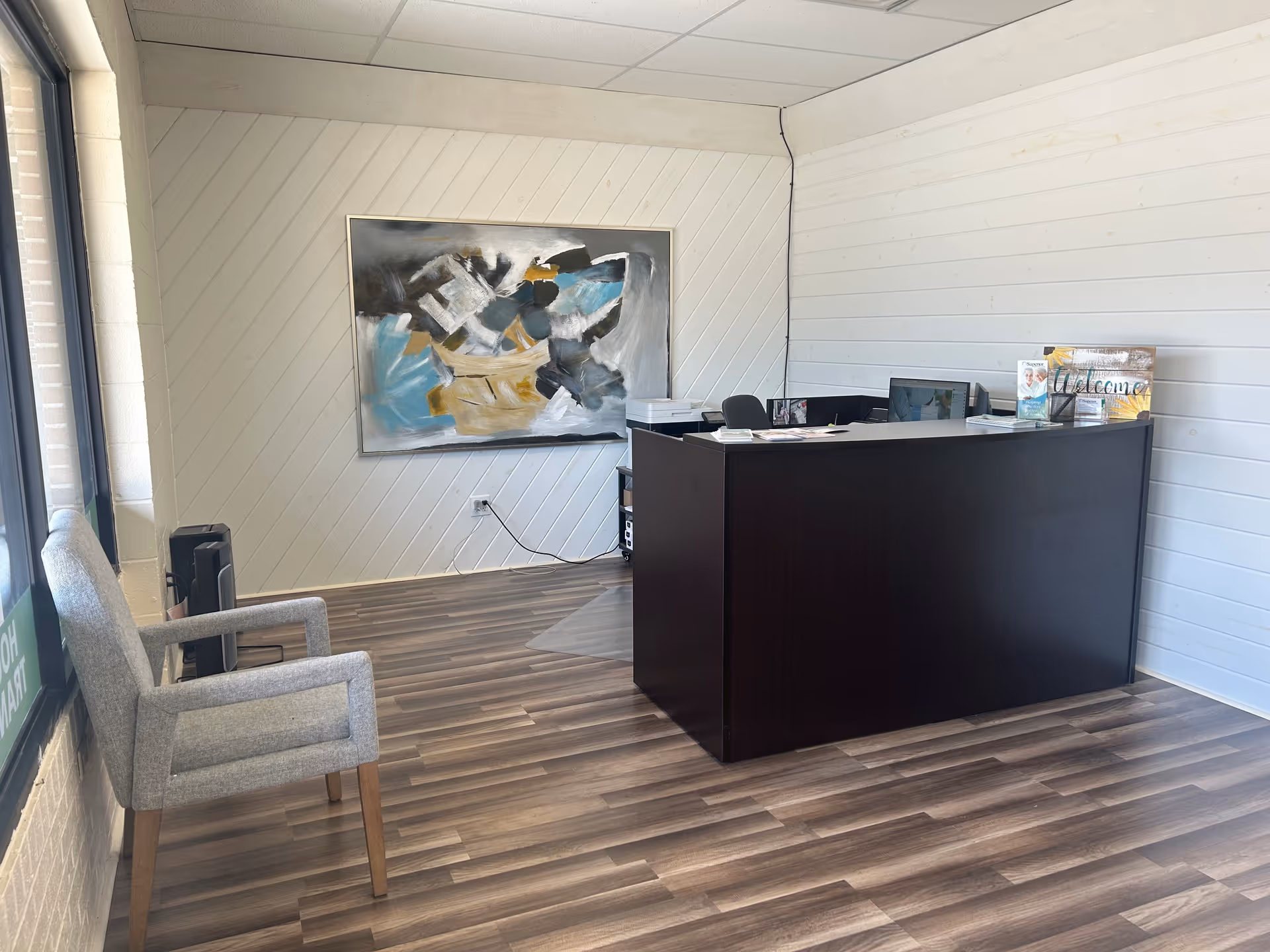 Reception desk in a bright lobby with abstract art and wood flooring.