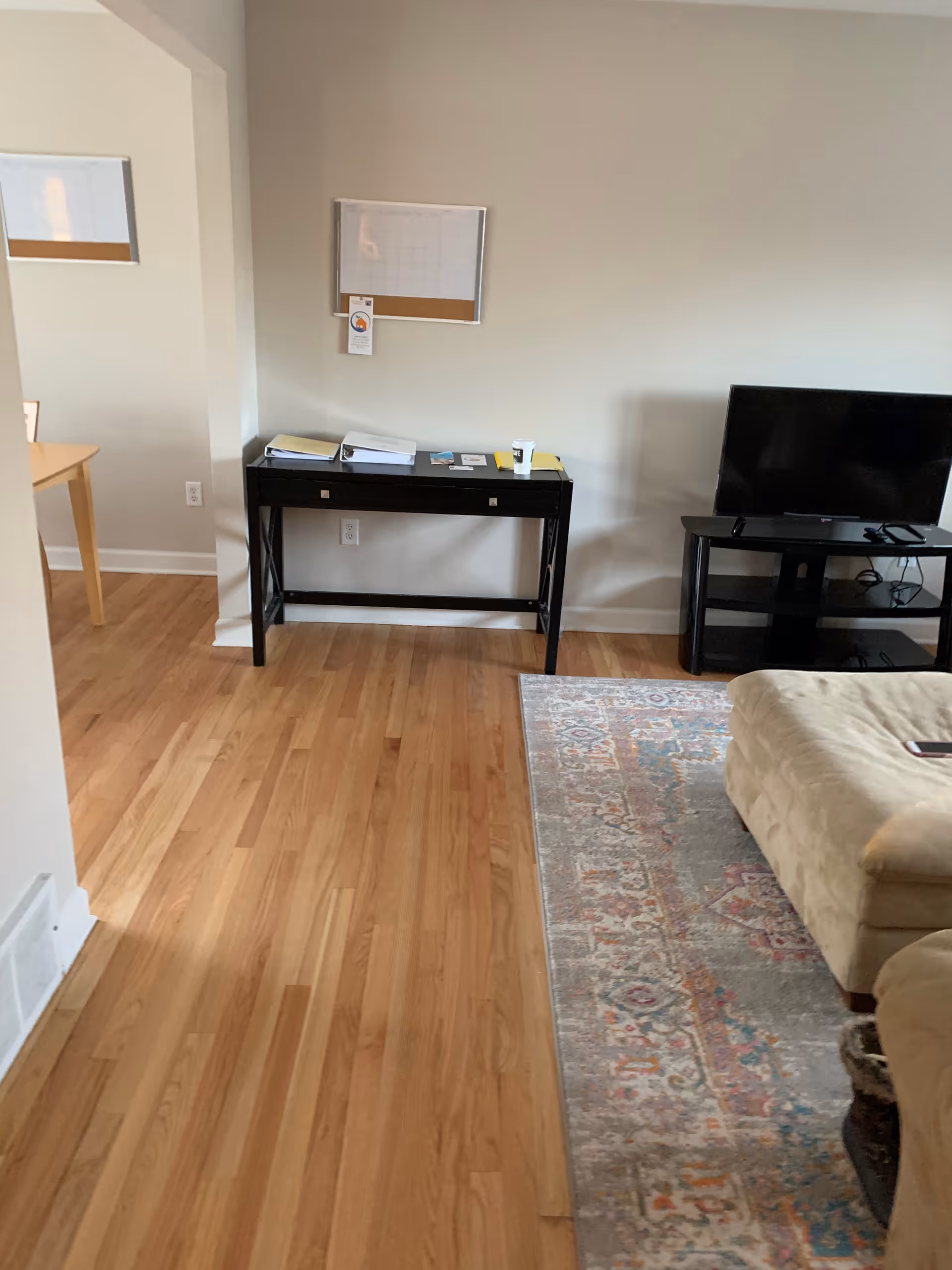 Living room area with a desk, TV stand, sofa, rug, and wood floor.
