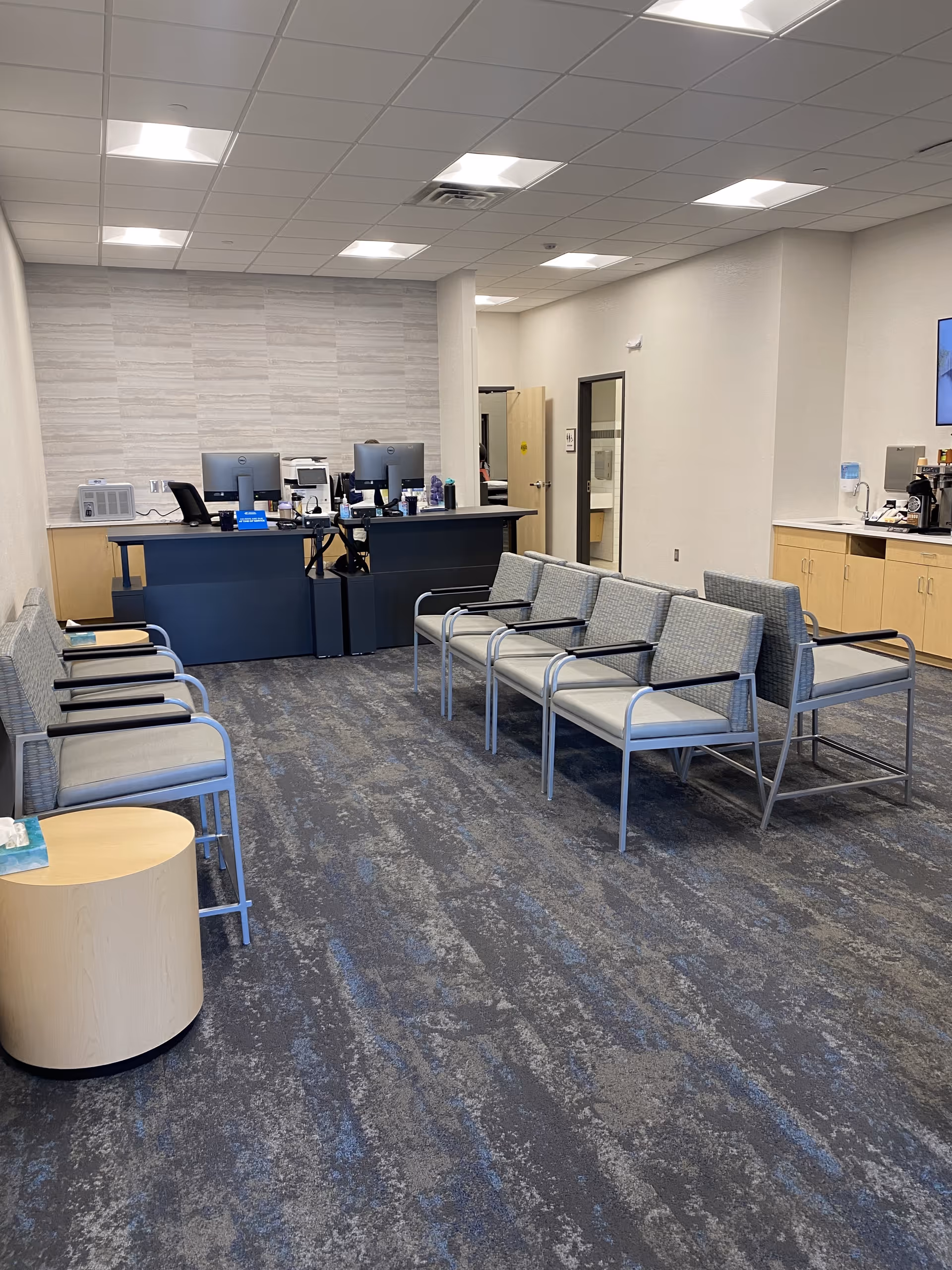 Reception area with blue front desk, multiple computers, and waiting chairs in a clean medical lobby.