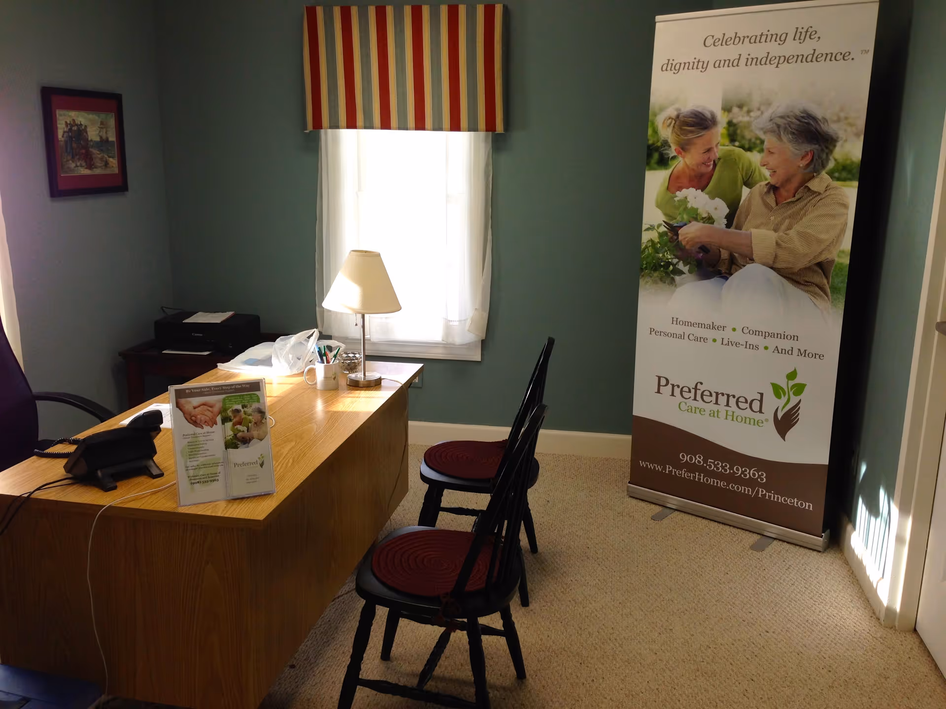 Office with wooden desk, lamp, chairs, window, and a tall banner.