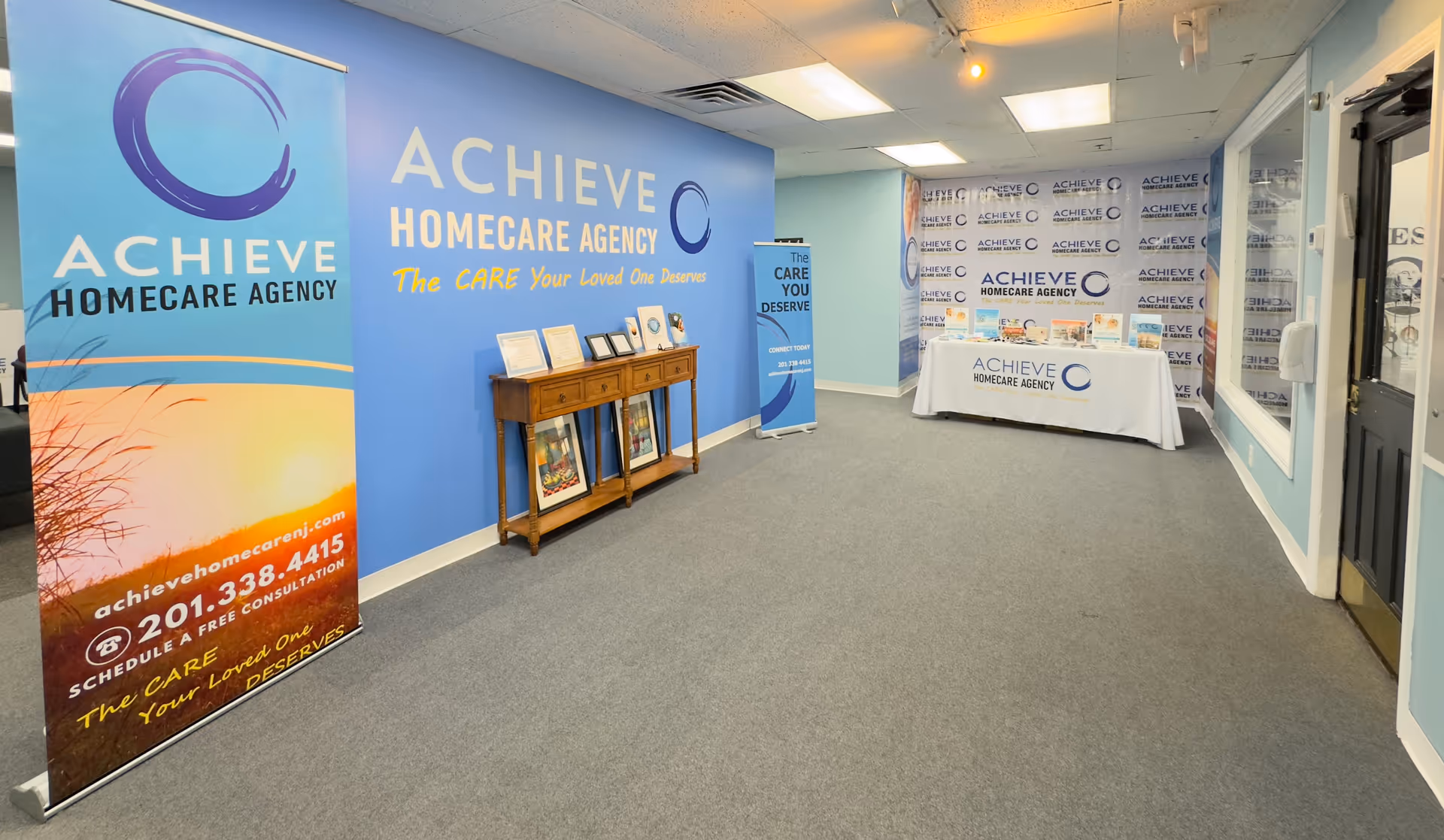 Indoor lobby with blue ACHIEVE HomeCare banners and framed displays along a wall