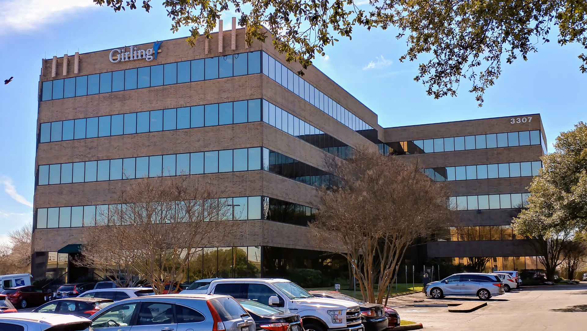 Brick, multi-story Girling Personal Care building with glass windows and a parking lot.