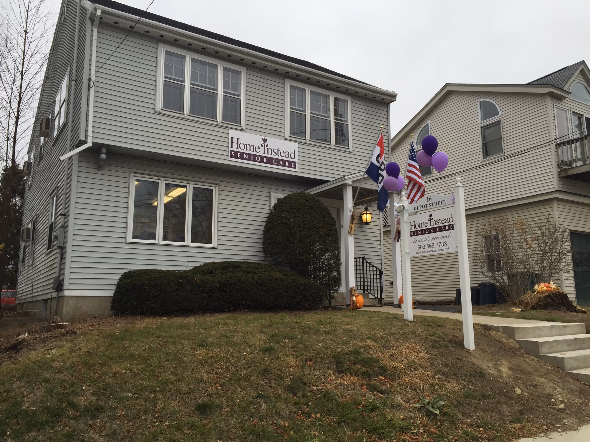 Two-story gray building labeled Home Instead Senior Care with a sign and purple balloons.