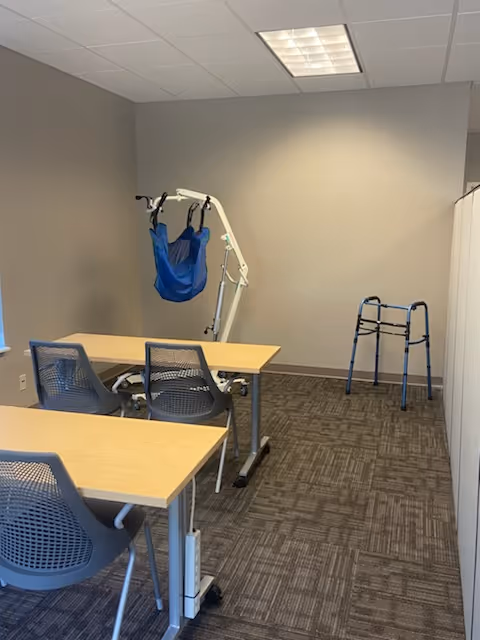 Interior room with desks and chairs, and a blue patient lift against the wall.