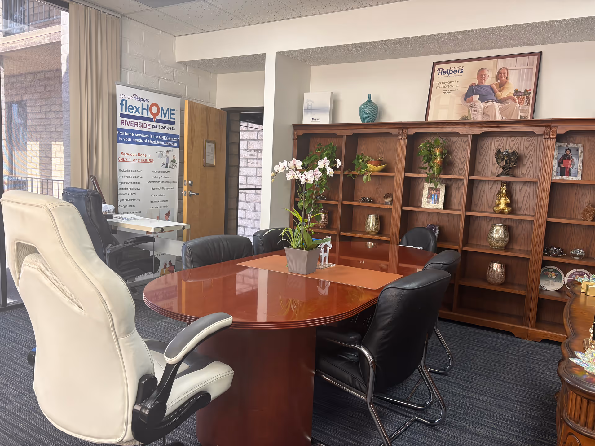 A conference room with a round table, mixed chairs, and a wooden bookcase.