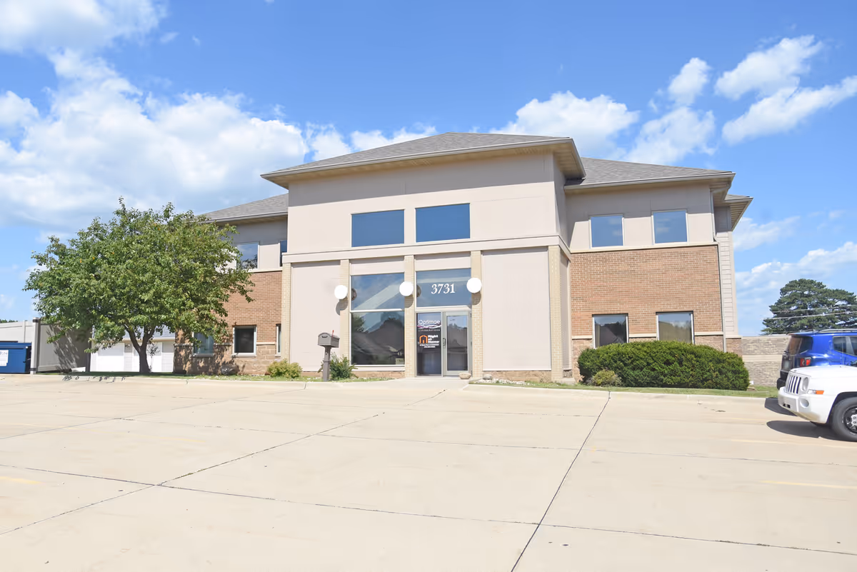 Modern beige and brick senior living facility with glass entrance and parking.