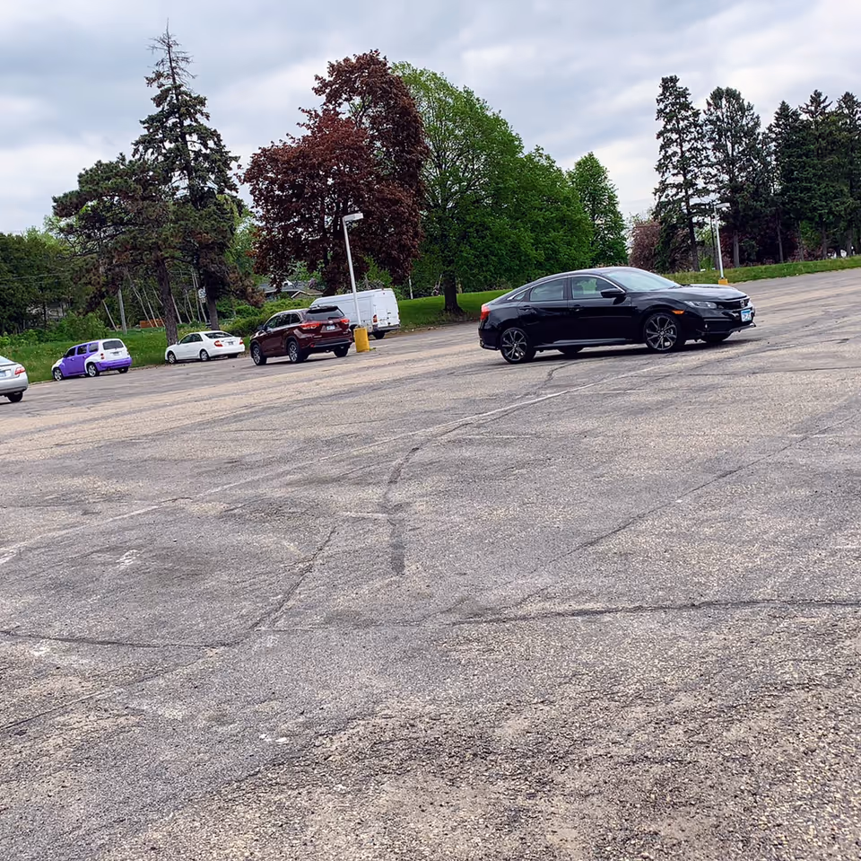 Outdoor parking lot with several cars and trees under cloudy sky.