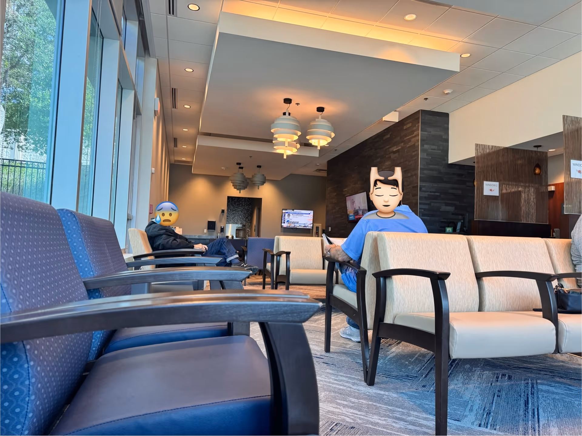 Modern medical center lobby with blue seating and large windows, two people seated.