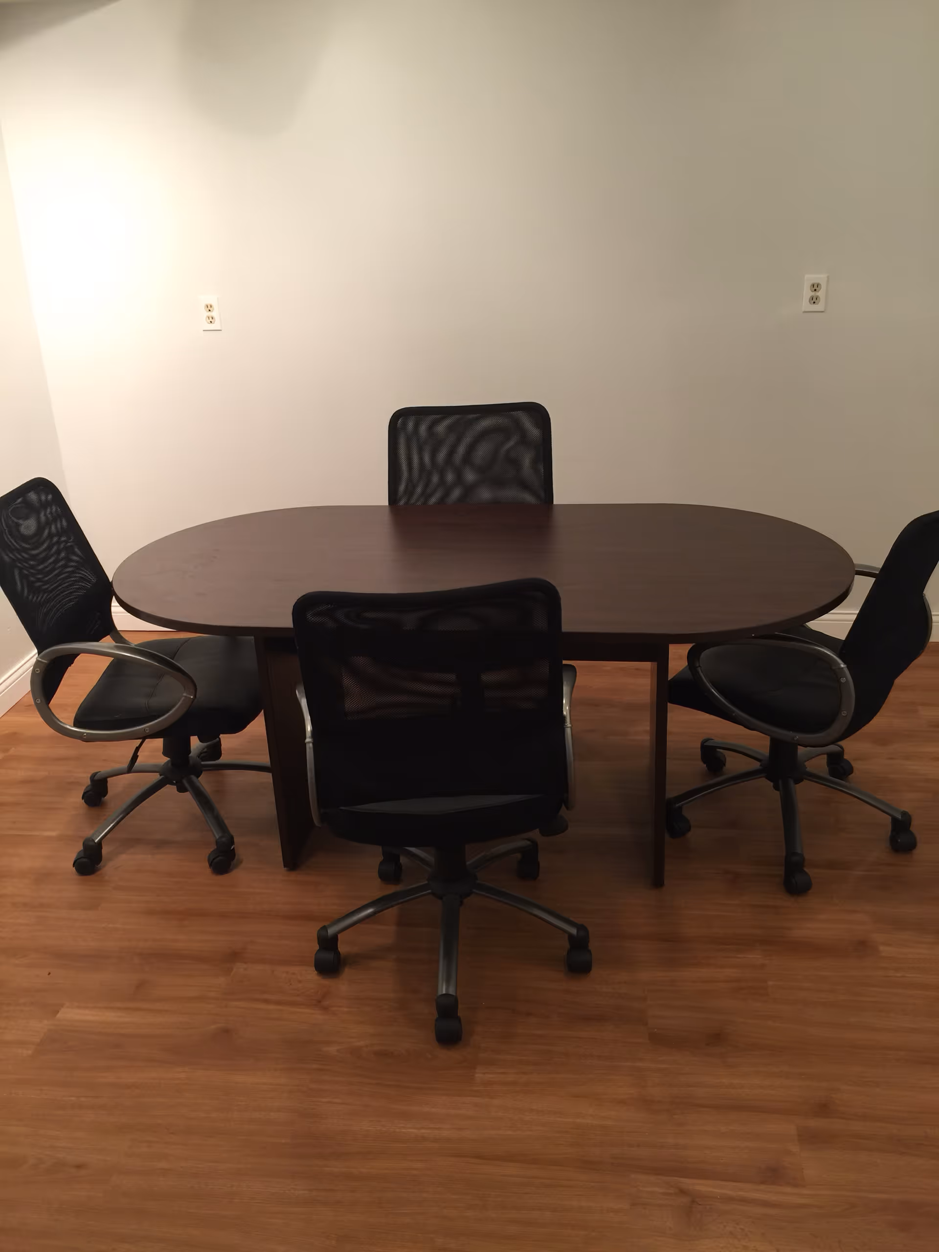 Empty interior conference area with a dark oval table and five rolling chairs.
