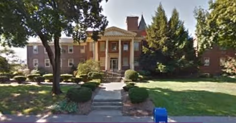 Front view of a brick senior living building with steps and trimmed landscaping.