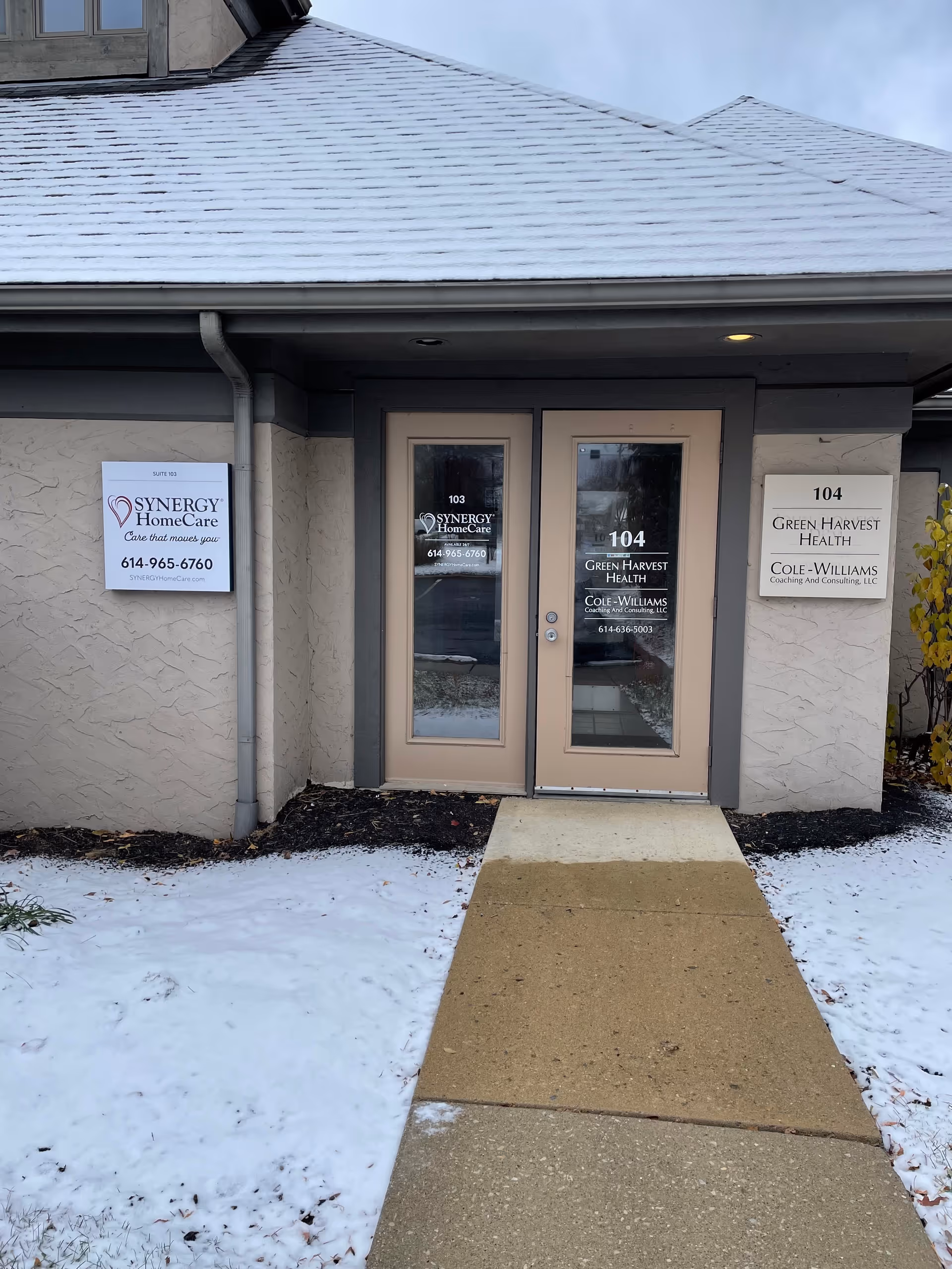 Entrance to SYNERGY HomeCare building, double doors with signs, snow on the ground.