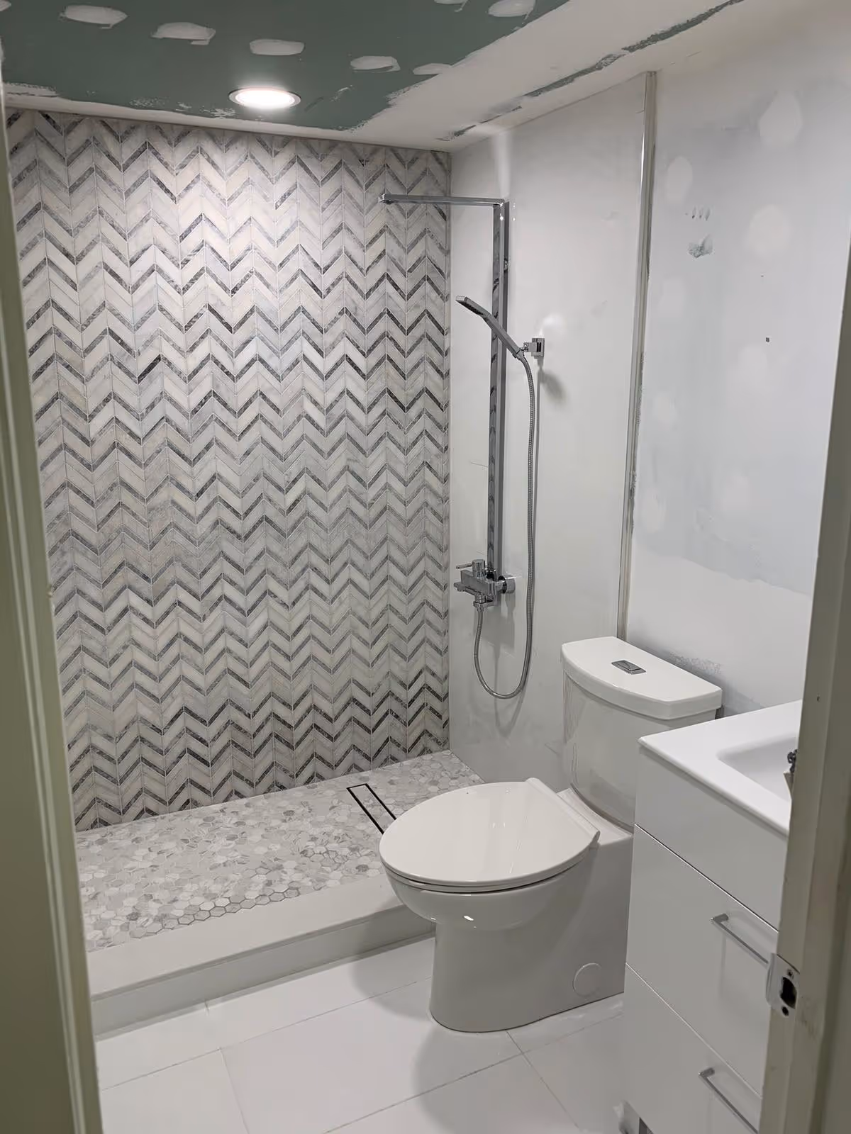 Modern bathroom featuring a tiled shower wall, toilet, and white vanity.