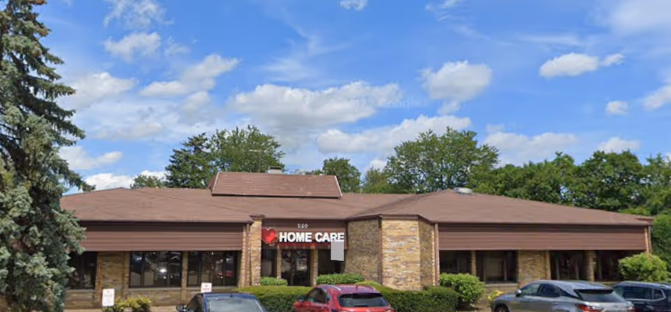 Exterior view of a single-story senior home care facility with brick facade and parked cars.