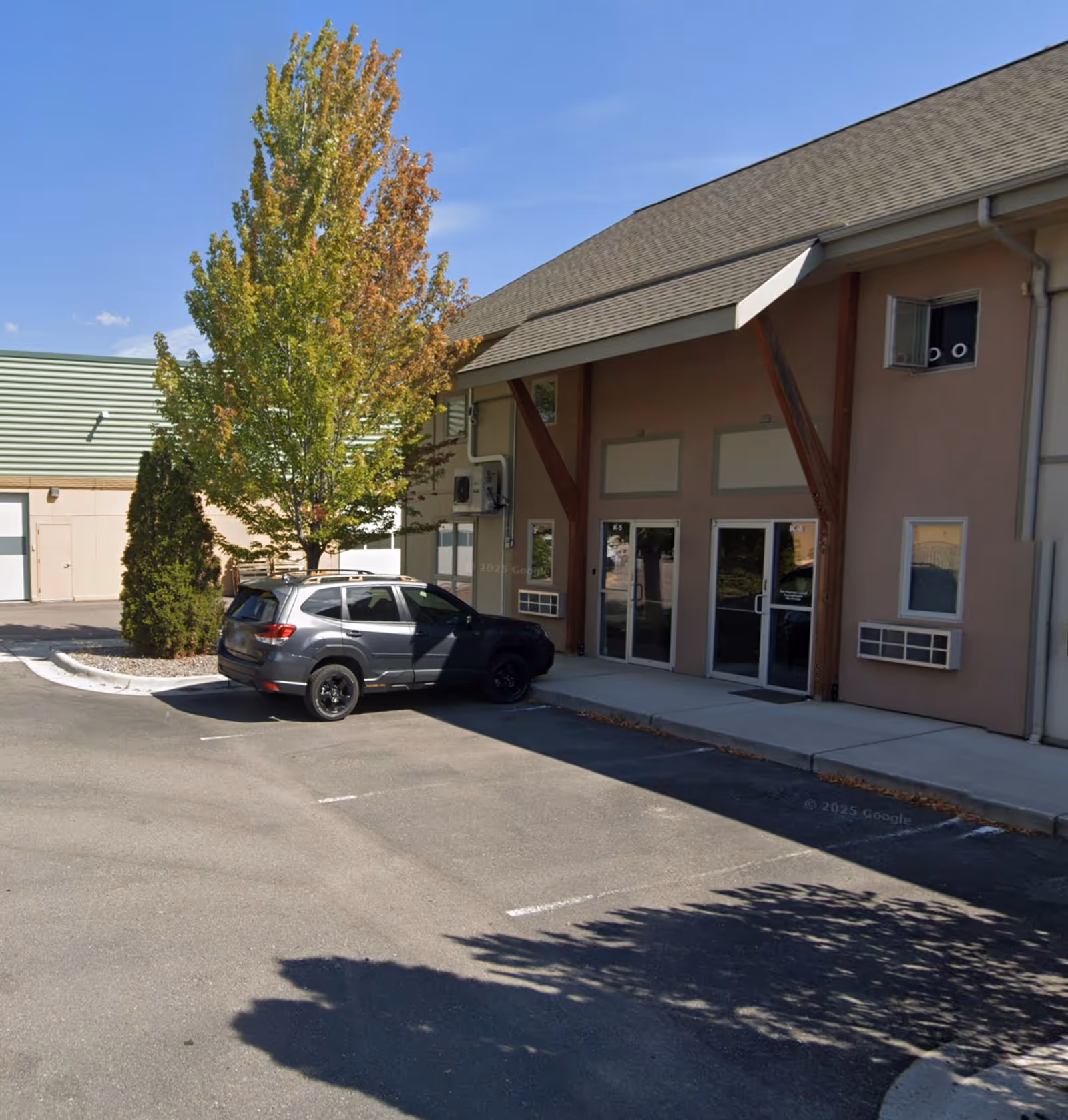 Exterior view of Home Instead building entrance with glass doors, parked car, and trees.