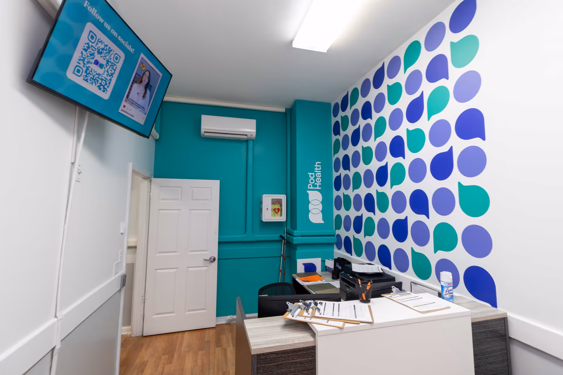 Reception desk in teal-walled office with dotted wall pattern and wall-mounted screen.