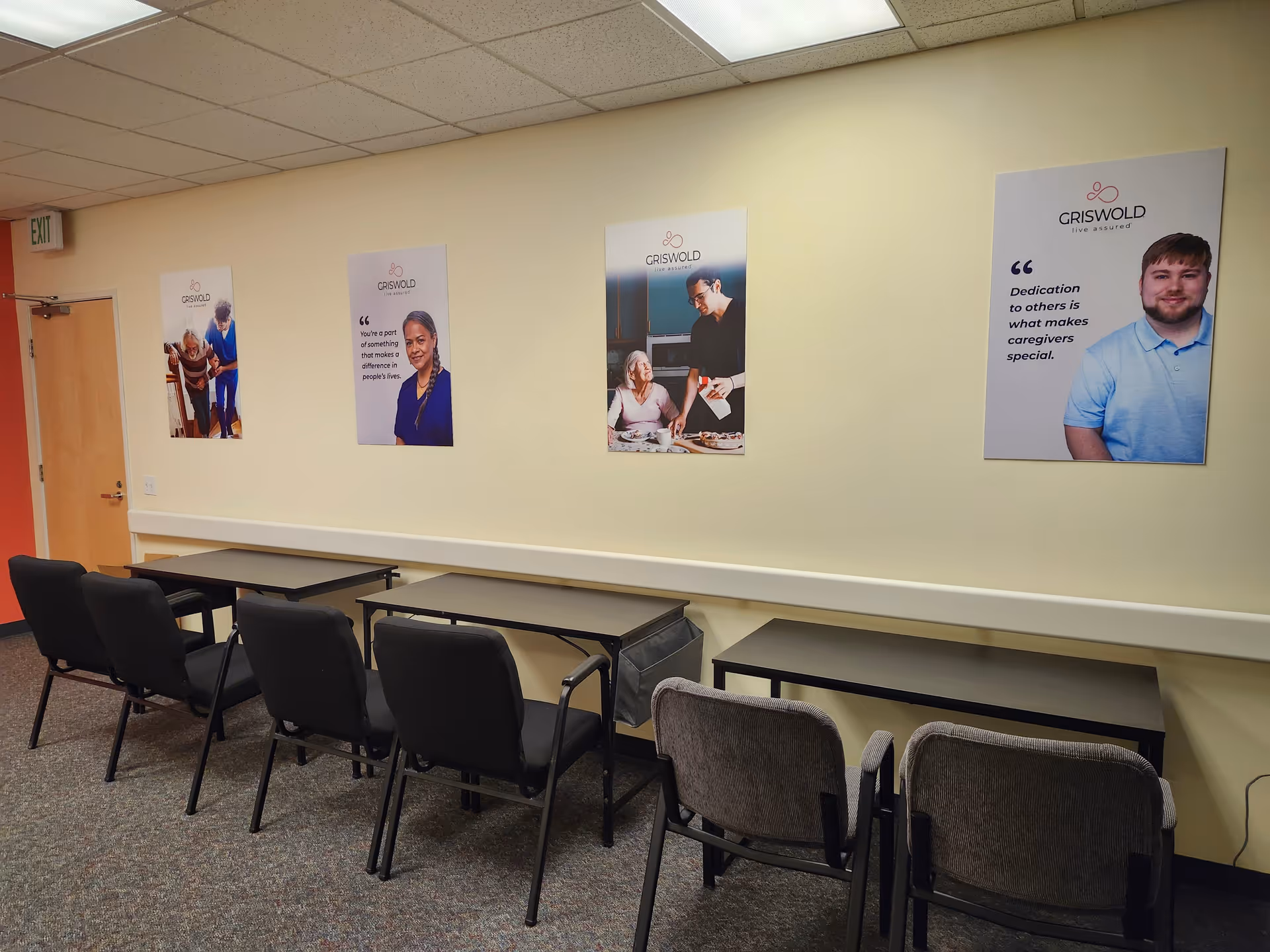 Room with a row of tables and chairs along a wall decorated by posters.