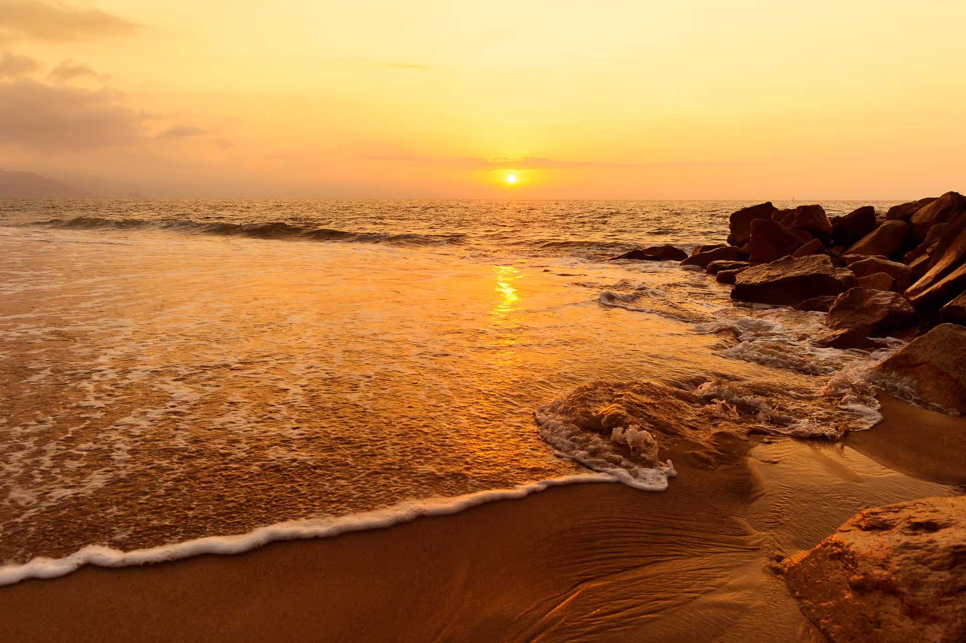 Sunset over a rocky beach with calm waves and golden hour light.