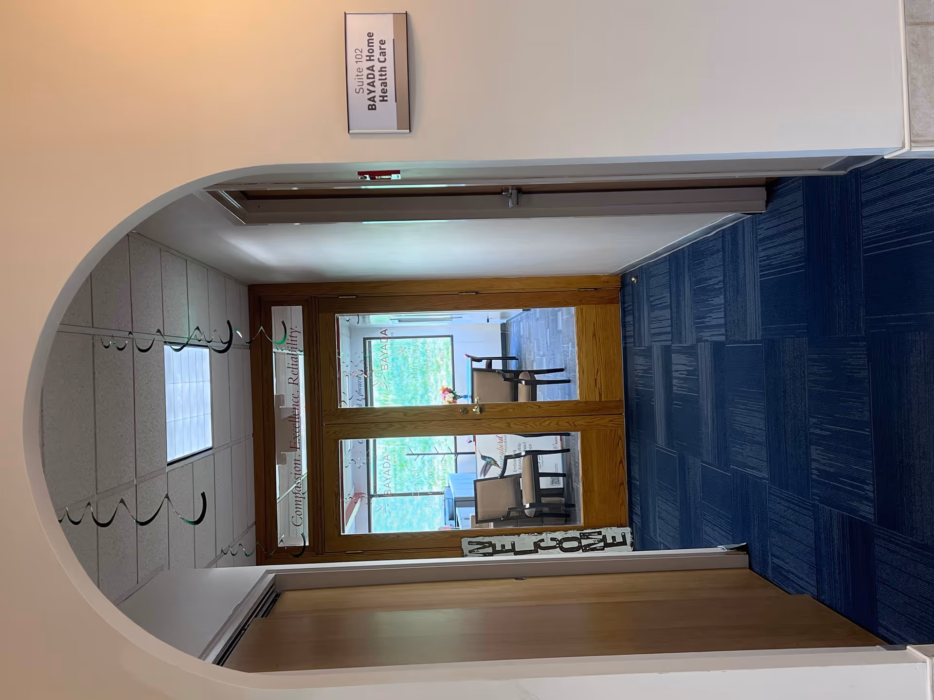 Interior hallway with arched entry, wooden doors, blue carpet, sign, and coat hooks.