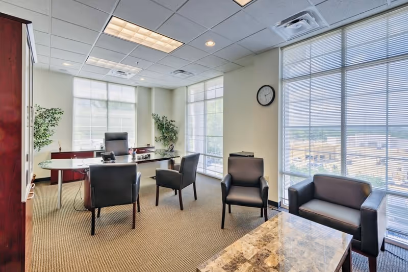An office-style reception area with a desk, chairs, and large windows in a senior living facility.